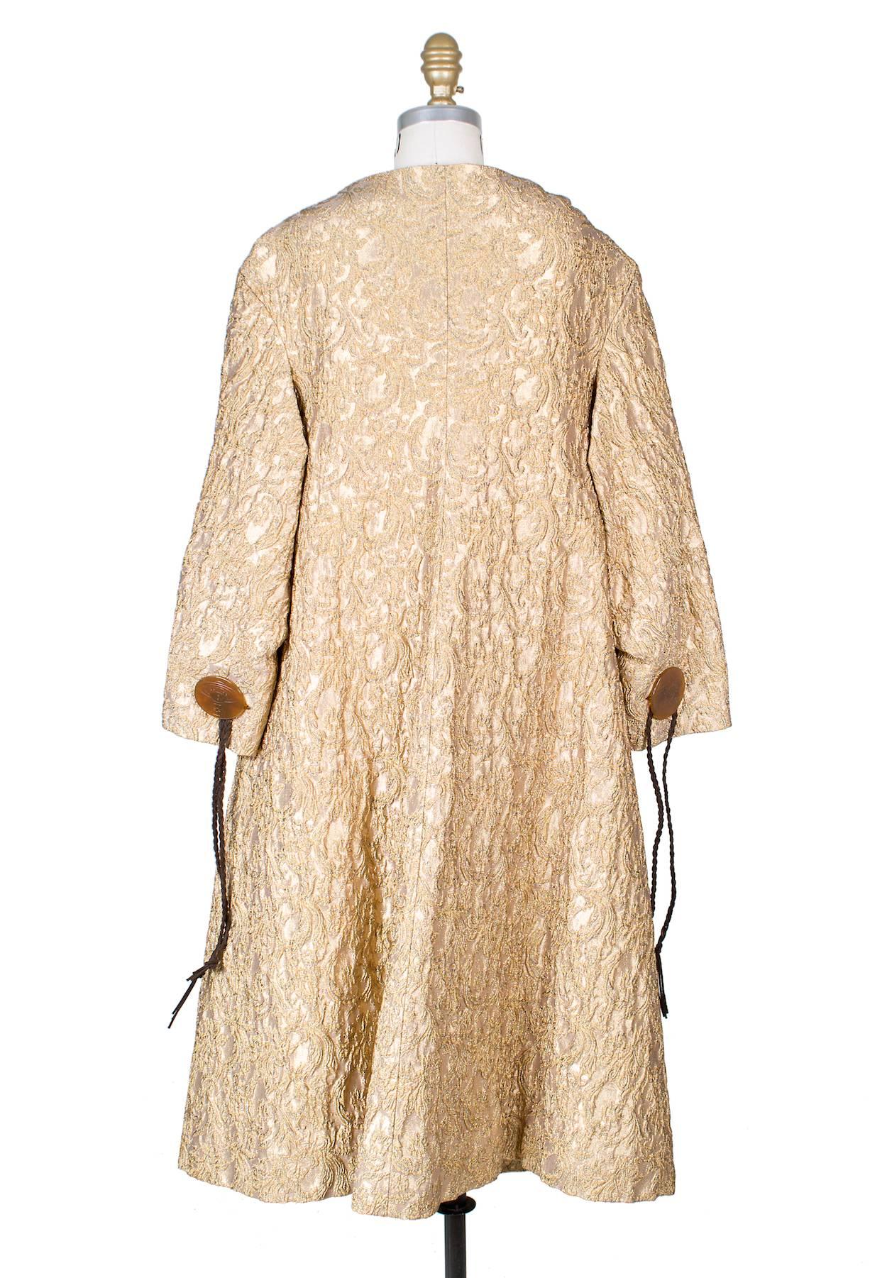 Coat by Vivienne Westwood.  It is made from a textured gold brocade fabric and features large buttons with braided suede strings and 3/4 sleeves.  It is lined in a quilted satin.  

18