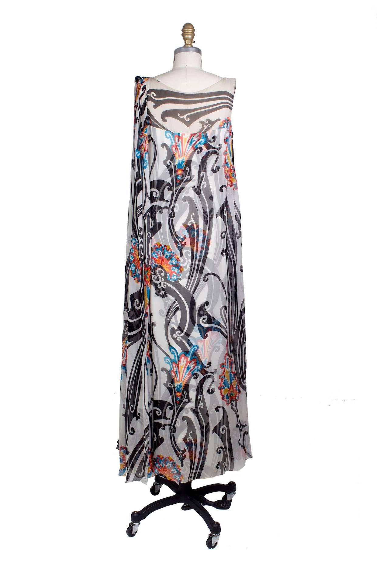 This is a dress with a sleeveless caftan by Malcolm Star c. 1960s.  It features a structured long sheath dress underneath covered by a sheer silk layer on top like a caftan which gathers on the left shoulder to create a drape.  Includes a tag inside