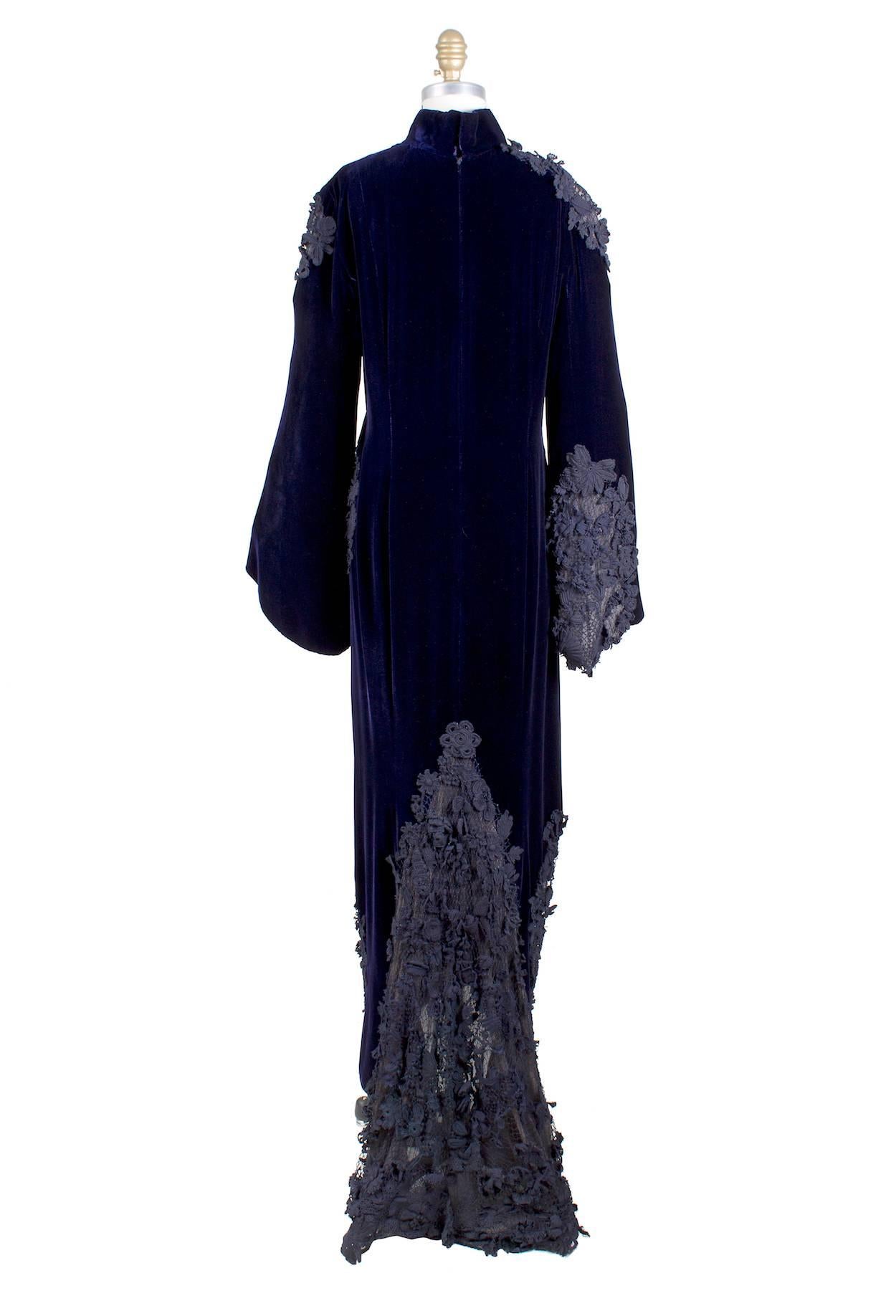 This is a couture dress by Jean Paul Gaultier c. 1990s.  It is made from midnight purple velvet and features black appliqués.  It has bell shaped sleeves and a dark purple chiffon lining.  The closure is a zipper in back with top snap and hook and