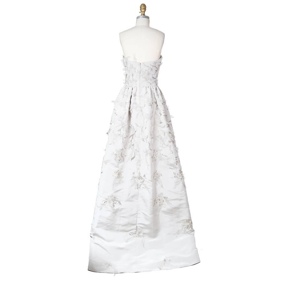 This is a dress by Oscar De La Renta.  It features an embroidered floral design with organza petal details.  It is constructed of heavy silk and includes a structured inner bustier and satin lined skirt.  The closure is a hidden zipper down the