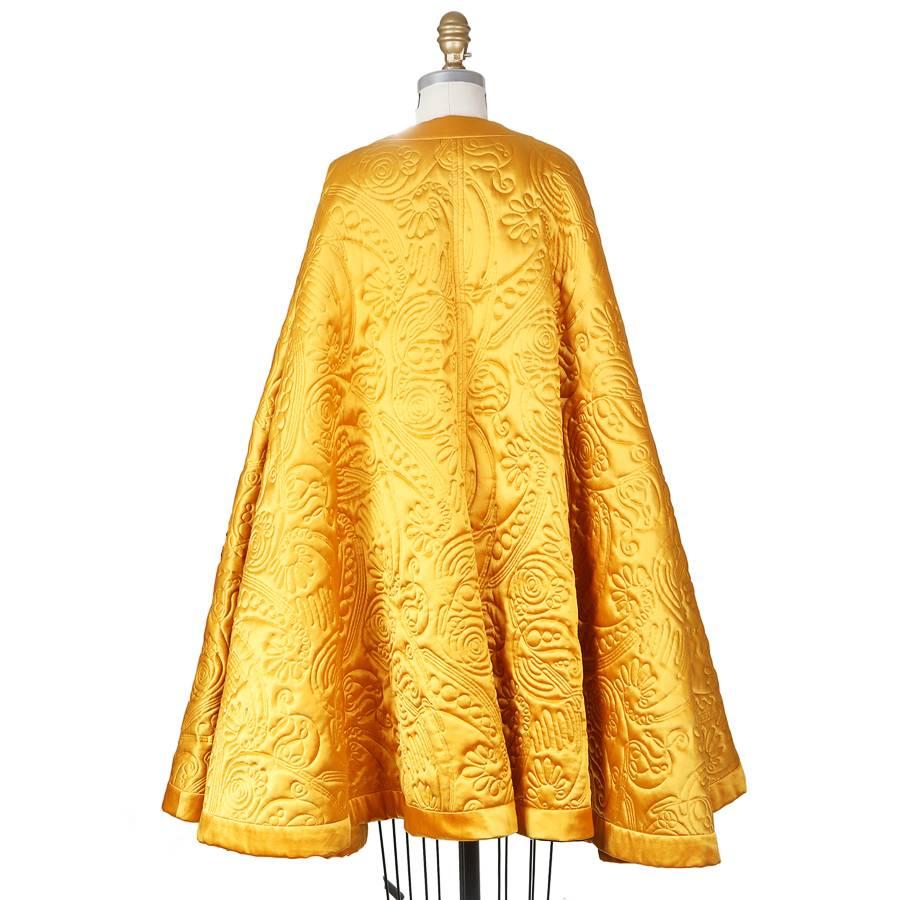 This is a cape by Yves Saint Laurent circa 1980s.  It is made from a yellow silk satin with a stitched quilting motif.  It has two closures in front (one over the bust and one at the neck) and has arm holes.  

When laid flat:
80