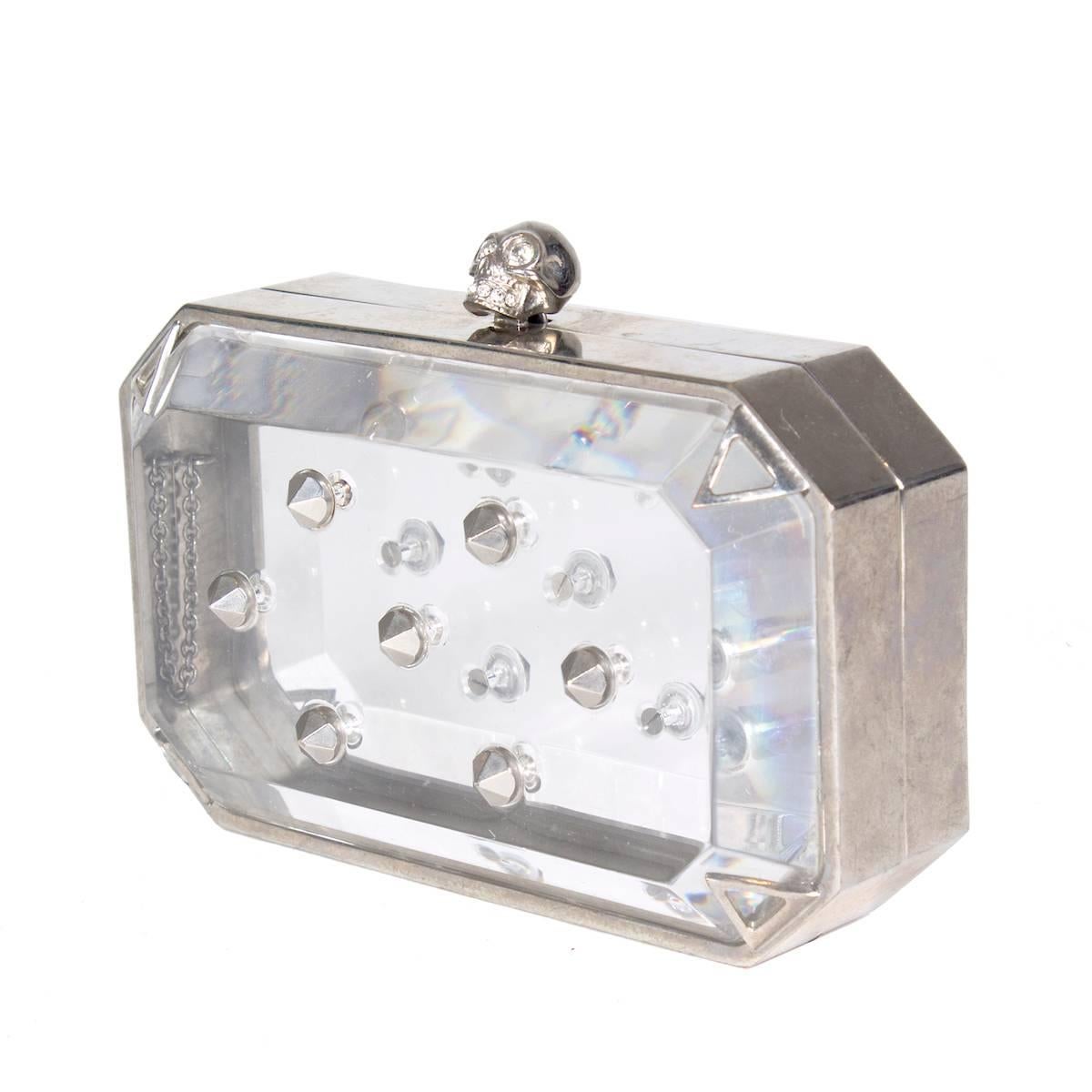 This is a clutch by Alexander McQueen.  It is a metal frame with clear lucite panels that are pierced with cone studs.  The top has a skull ornament toggle closure. 