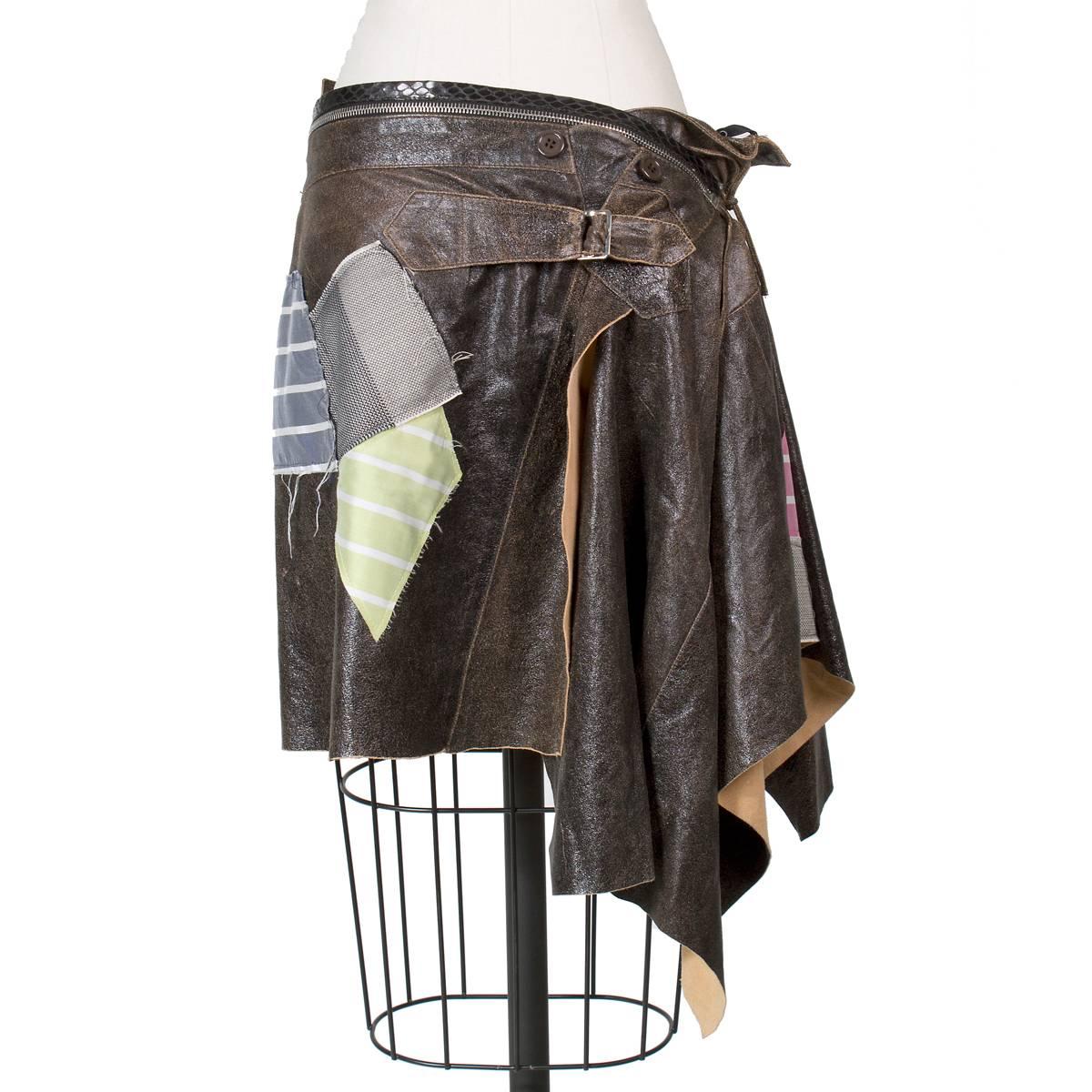 This is a skirt by John Galliano for Christian Dior circa early 2000s.  It features brown leather with a sheen and multiple sewn on patches.  There is a zipper around the waist and leather string ties on the side.
