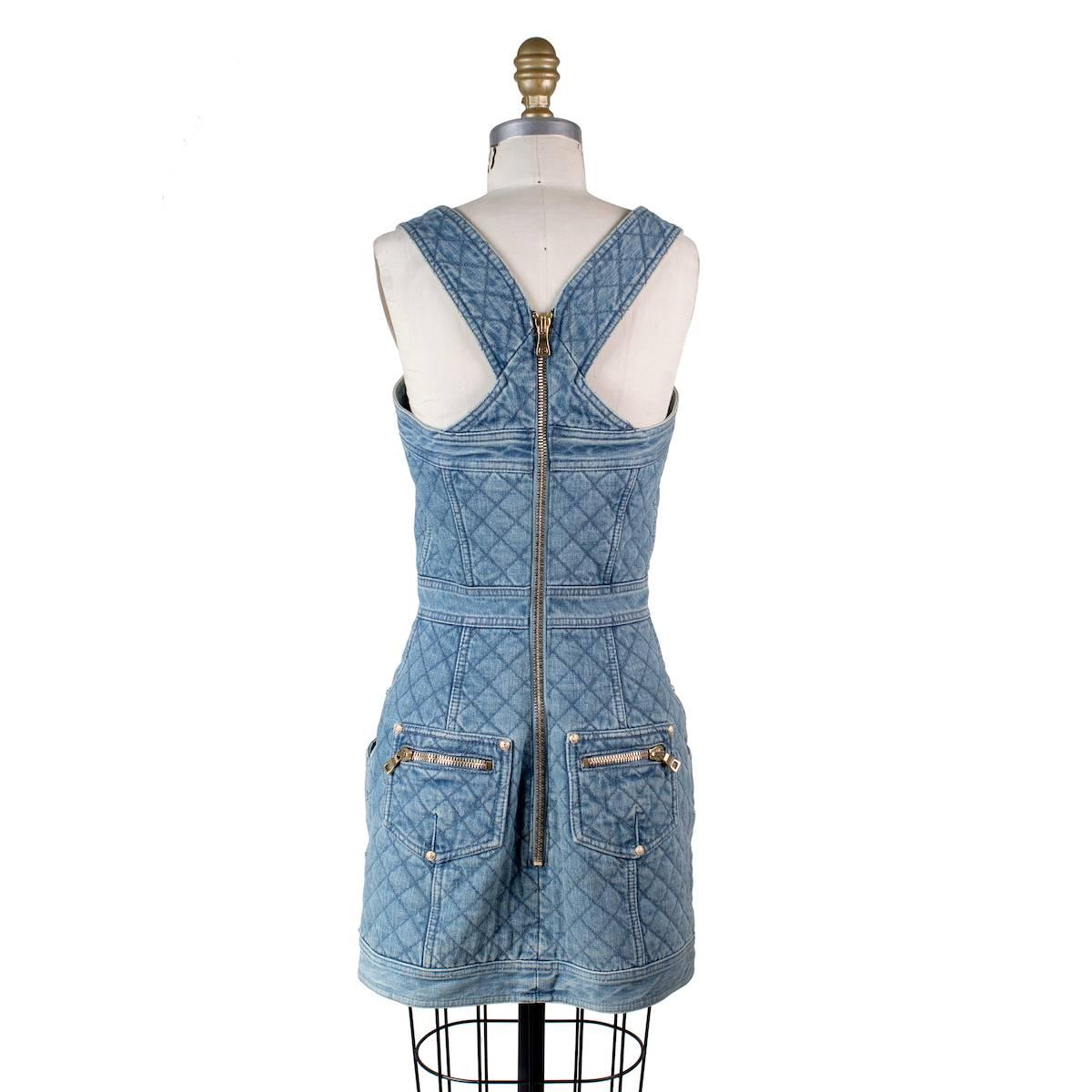 This is a dress by Balmain. Quilted light blue wash denim in overalls style.  Features gold buttons and hip pockets. Back zipper closure.