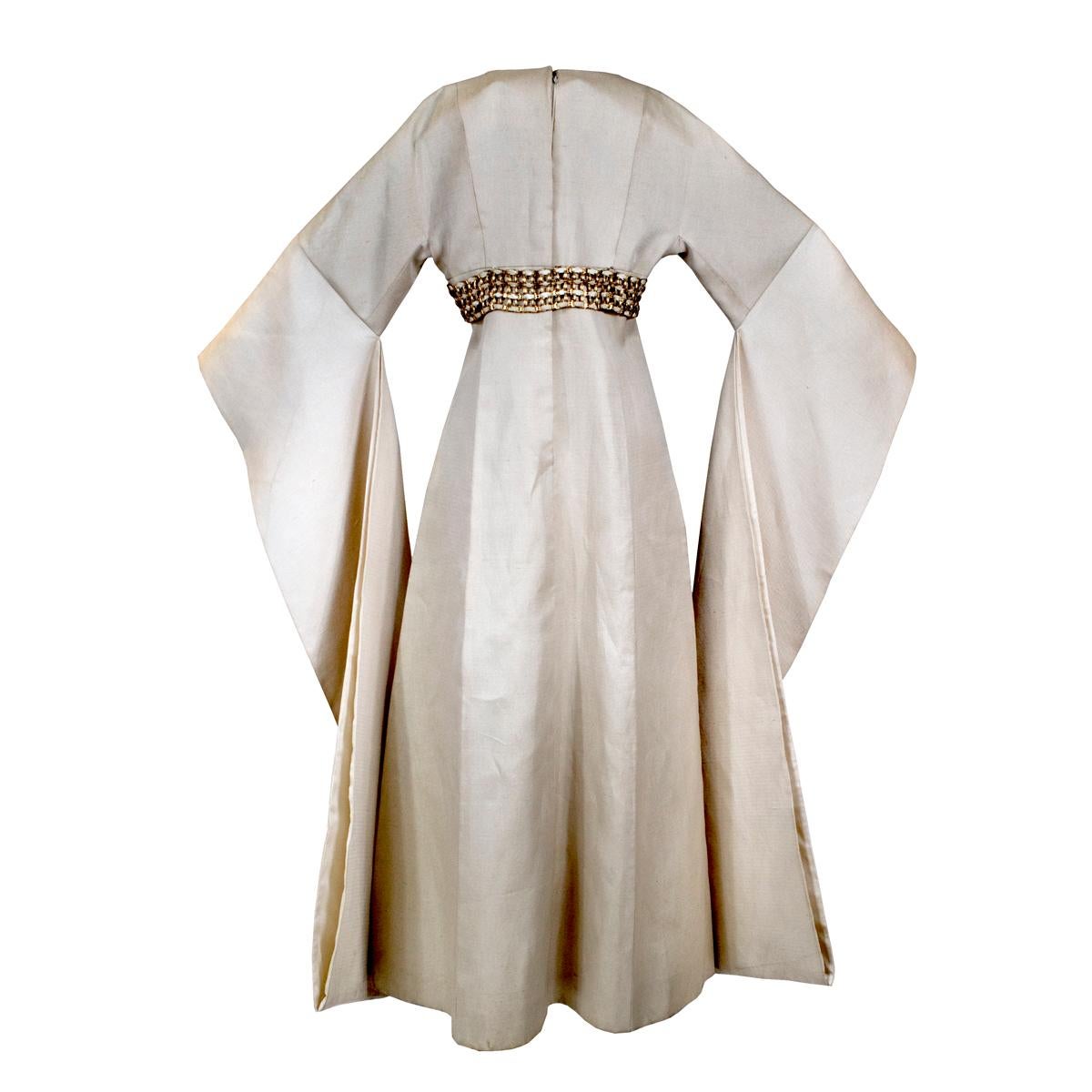 Kimono by Chester Weinberg c. 1965
Made from a rigid bone linen with a silk weave (natural beige color)
Organdy silk lining
Empire waist
Metal chain link / weave belt
Back zipper closure with top hook and eye

Size/measurements:
36