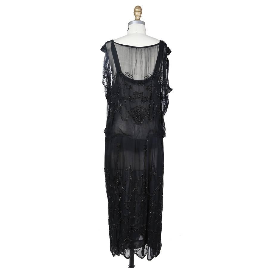 The is a black chiffon shift dress c. 1940s.  The designer is unknown due to it’s age and lack of a tag.  The dress includes a chiffon slip that is covered by a layer of chiffon with swirled pattern of black beads. The closures are snaps on the side.