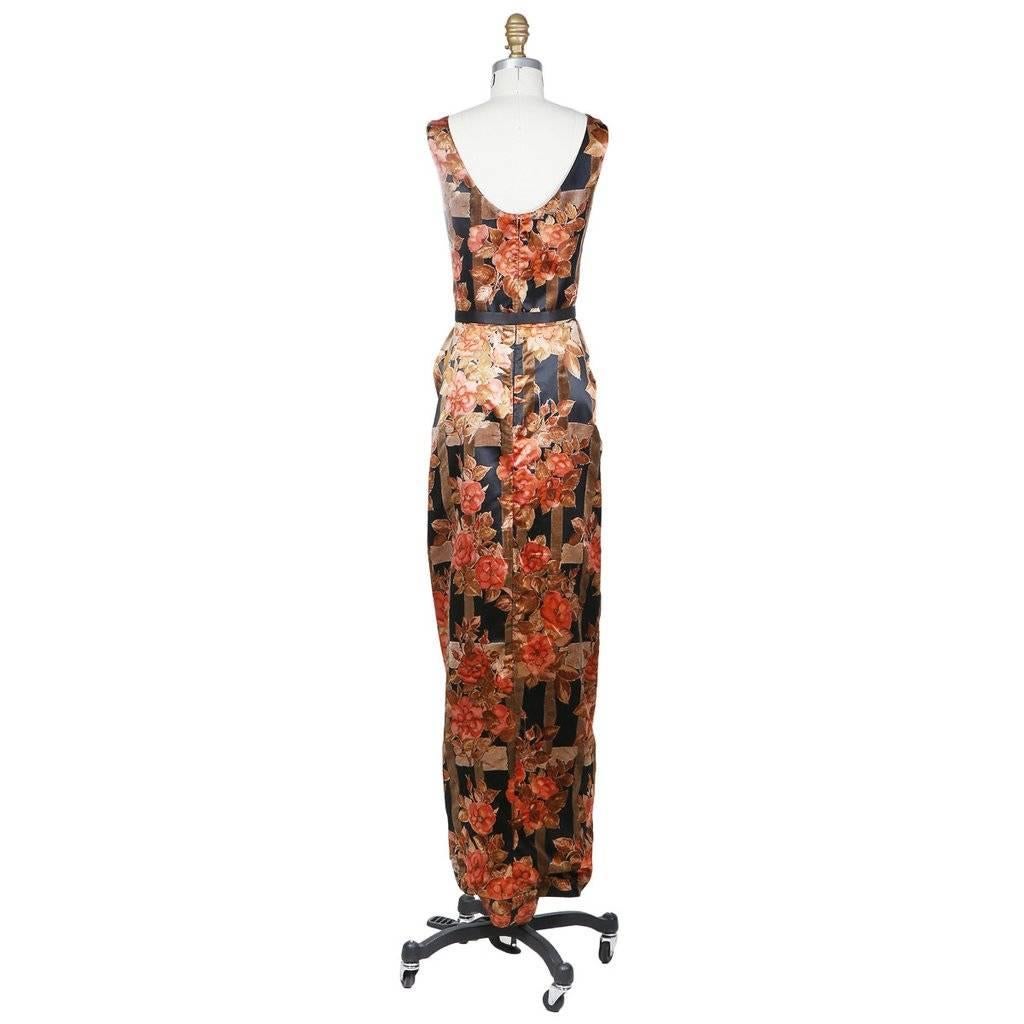 This is an evening dress by Galanos c. 1960s.  It features a warm toned floral print with rich pinks and browns against a black background.  The dress includes a black satin belt with a bow in front.  The belt cinches the dress the create shape and