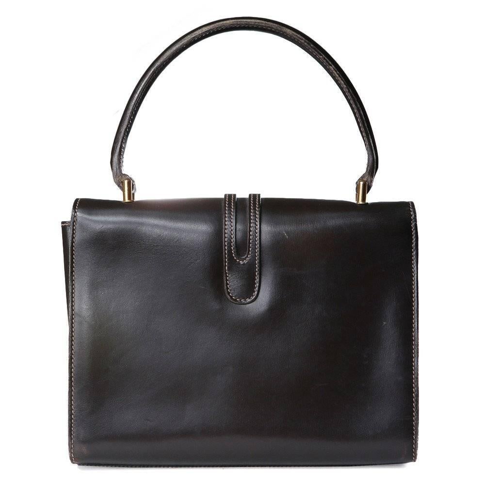 This is a black leather handbag by Gucci c. 1970s.  It features gold hardware, twist lock, contrast stitching, leather piping on flap, two open pockets, and one zipper pocket.
Length is 9"
Height is 4"
Width is 3"
Shoulder drop is