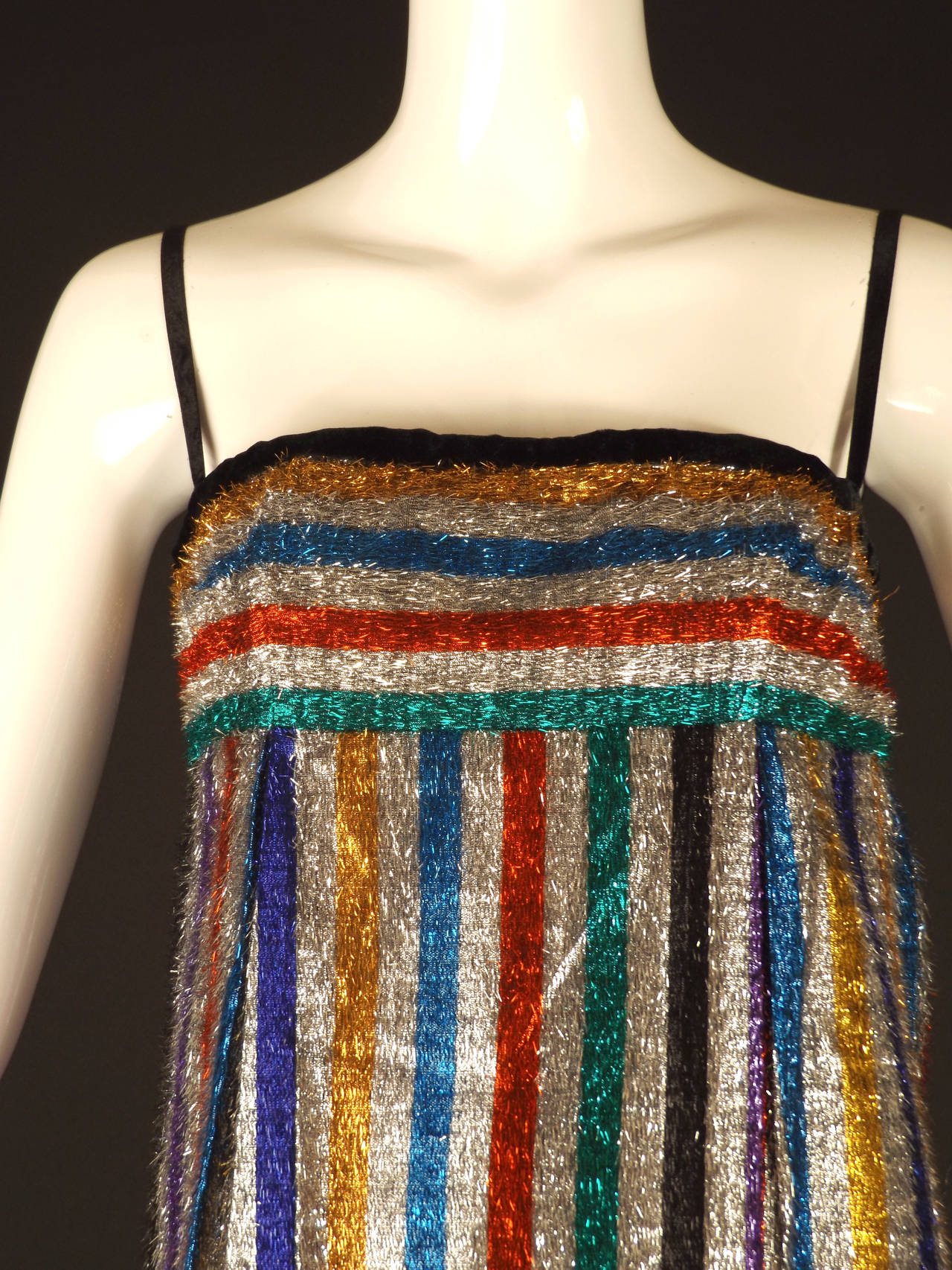 FABULOUS 1960s evening dress in a stripe eyelash lamé. The stripes are silver with a red, black, green, purple, turquoise and yellow. Black velvet ribbon shoulder straps and binding along the top edge. The dress has an Empire waistline and is dart