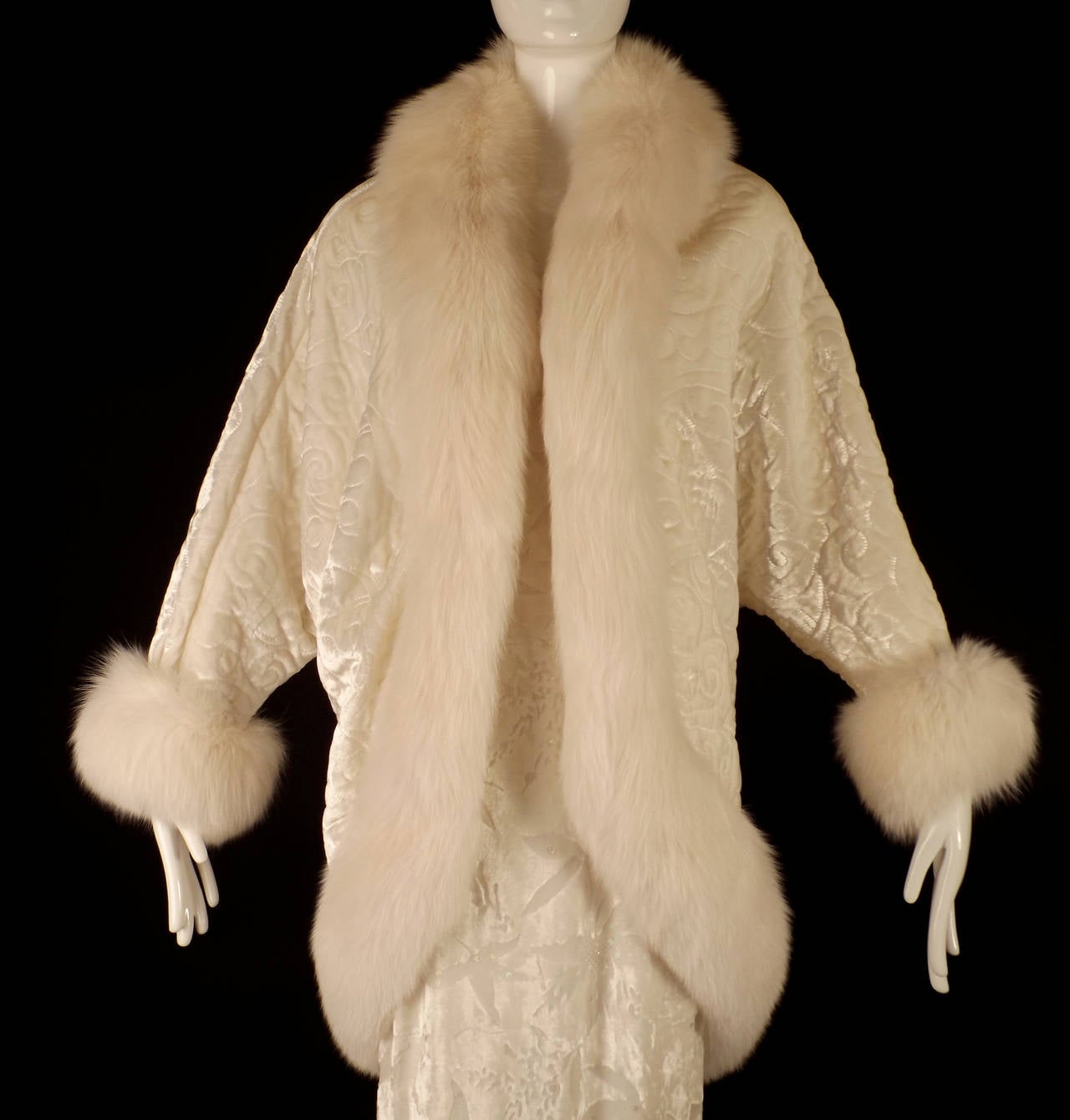 Fantastic cocoon evening coat very reminiscent of the 1920s in white quilted velvet and trimmed in white fox fur.  The coat has a scrolling pattern in the quilting and it's lined in white silk crepe back satin. The coat is trimmed in the most