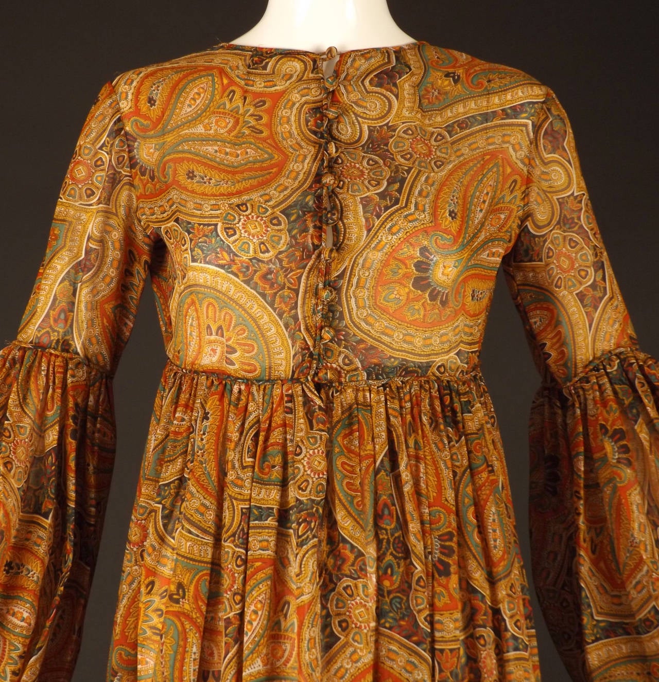 Fabulous boho chic peasant dress from c.1970 in a lightweight paisley printed wool gauze.  The colors are red, orange, white, green and black. Covered button closures down the front of the dress to the slightly raised, piped waistline. Long, set in