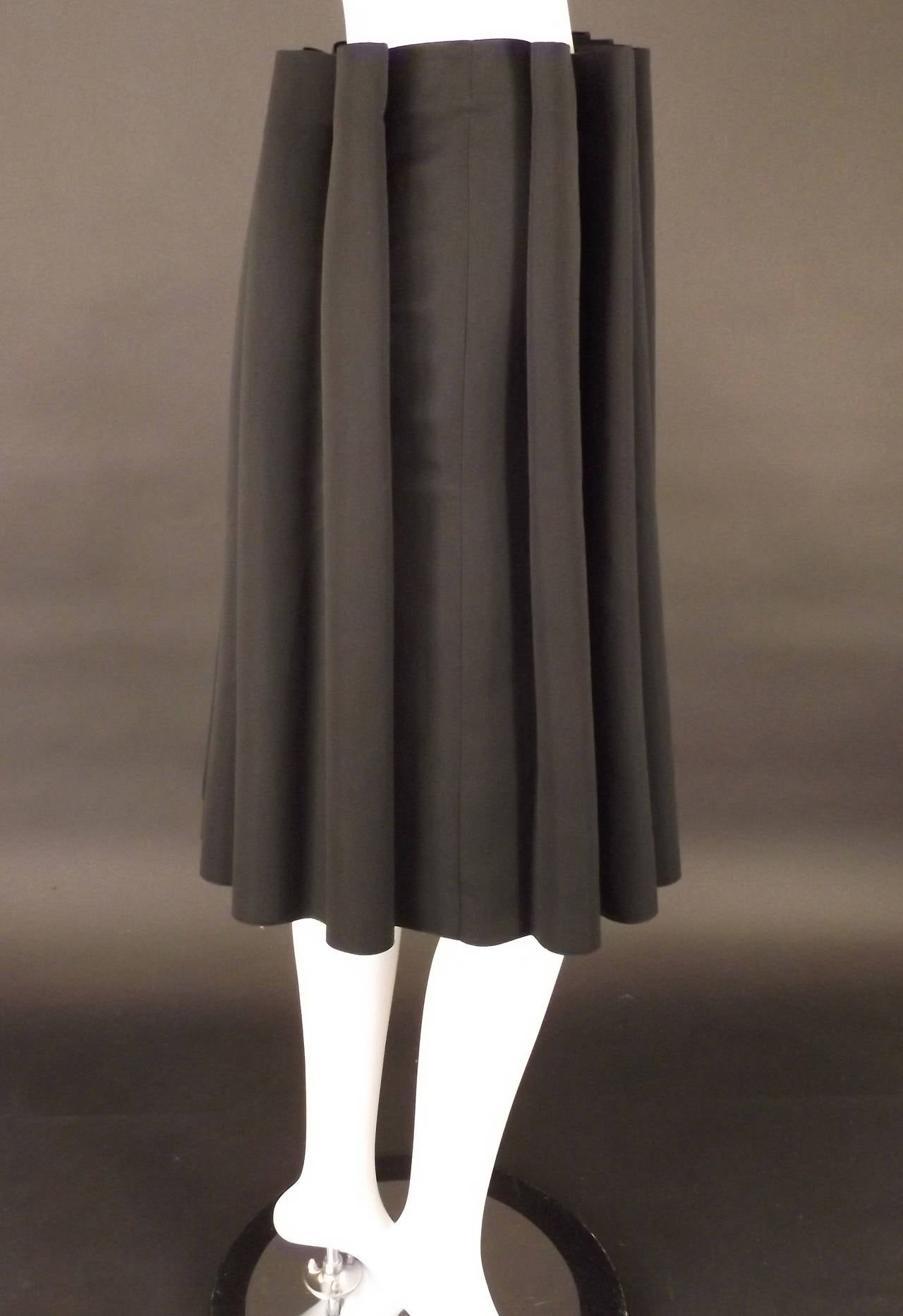 Amazing skirt in black polyester satin. The skirt has released, outward pointed tucks that are not flattened, but are rolled instead, creating coils. The coils open into the body of the skirt creating fullness. Side zipper closure and unlined.