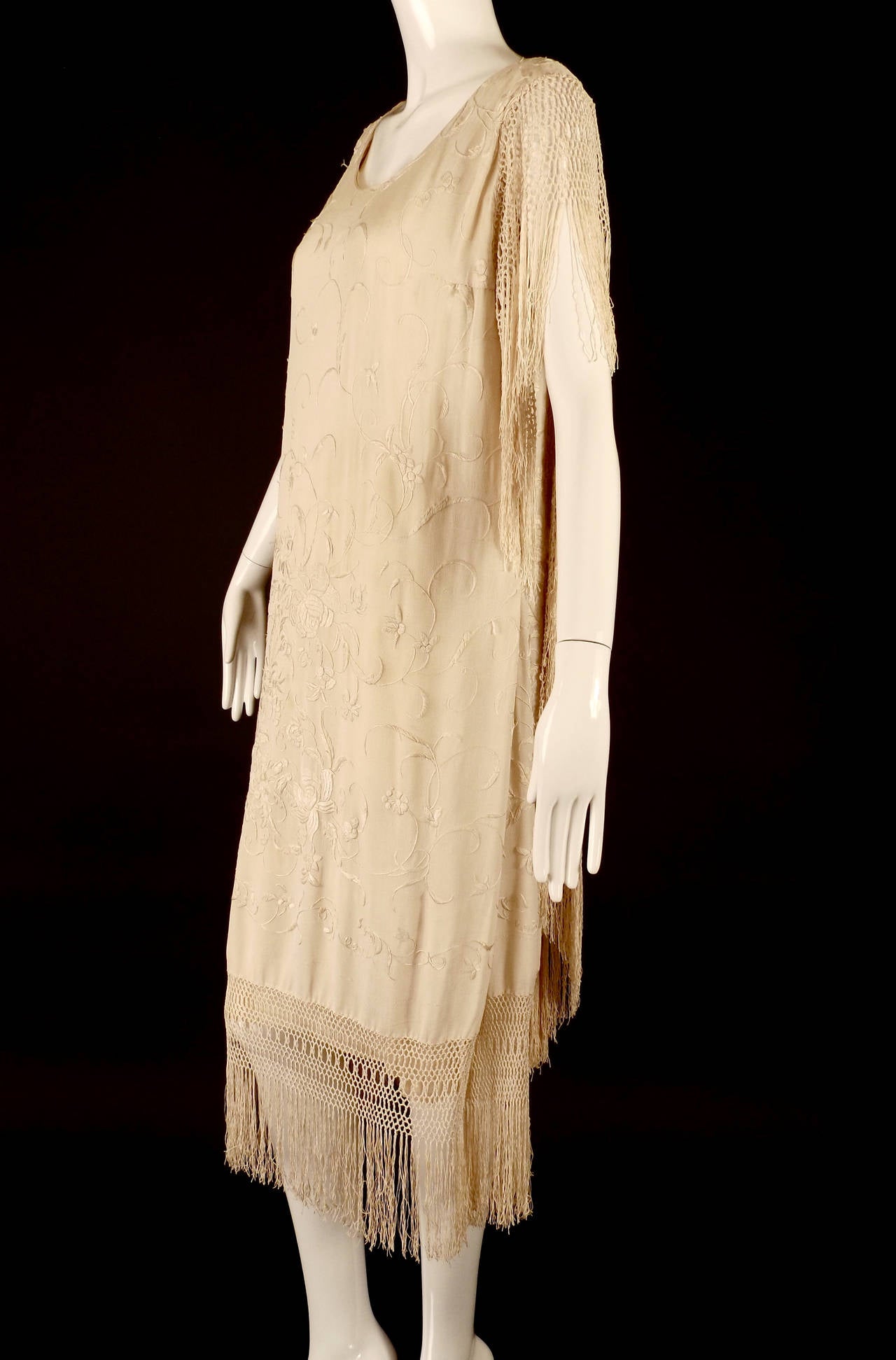 Stunning c.1924 evening dress made from silk fringe piano scarves. Okay the piano scarf…..It is an off whtie silk crepe with a gorgeous floral embroidery pattern. Hand tied fringe falls from the armscyes and along the hemline. The gown has a low