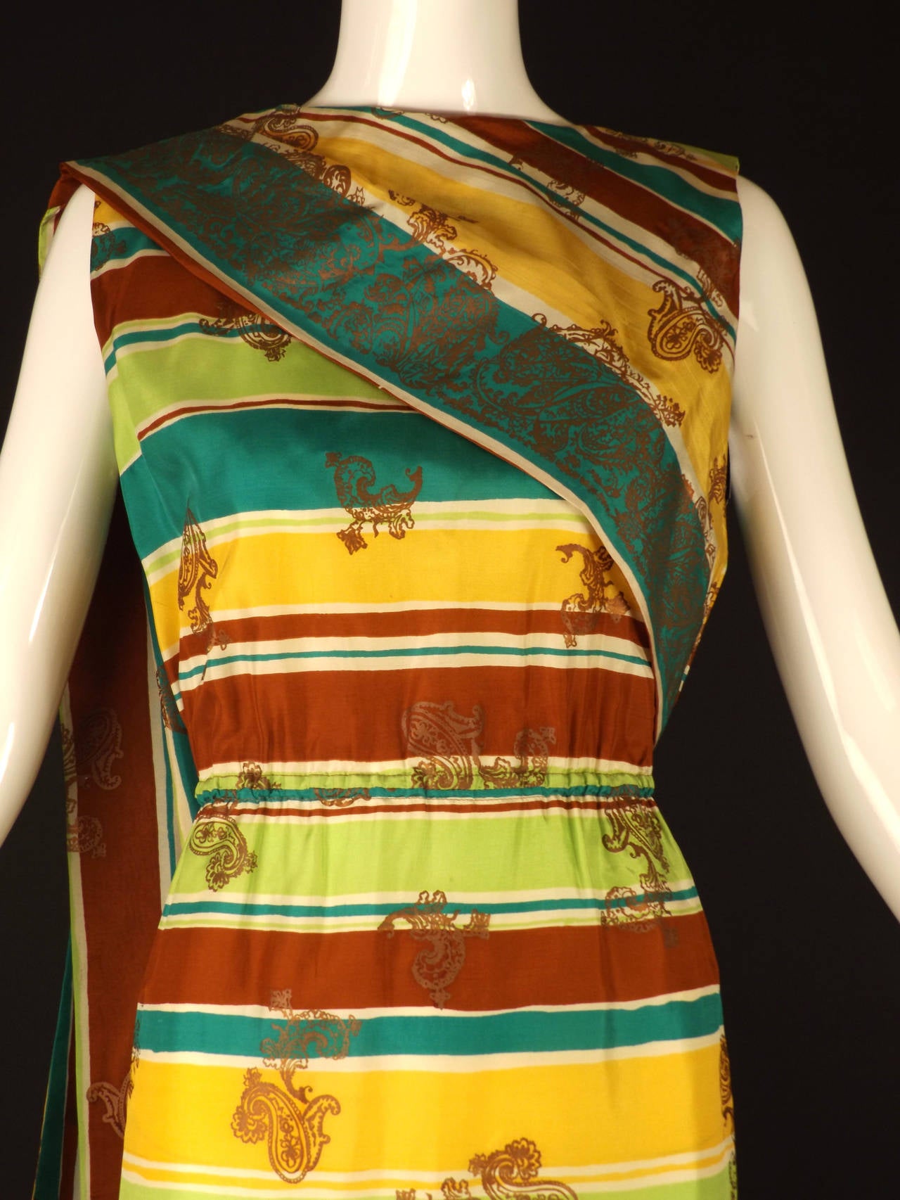 Wonderful shift dress in a china silk with a Tibetan flare. The silk has a stripe in white, brown, lime green, green and yellow and then has a matte gold paisley screen print. The dress has a scoop neckline and a  flat front bodice that falls to the