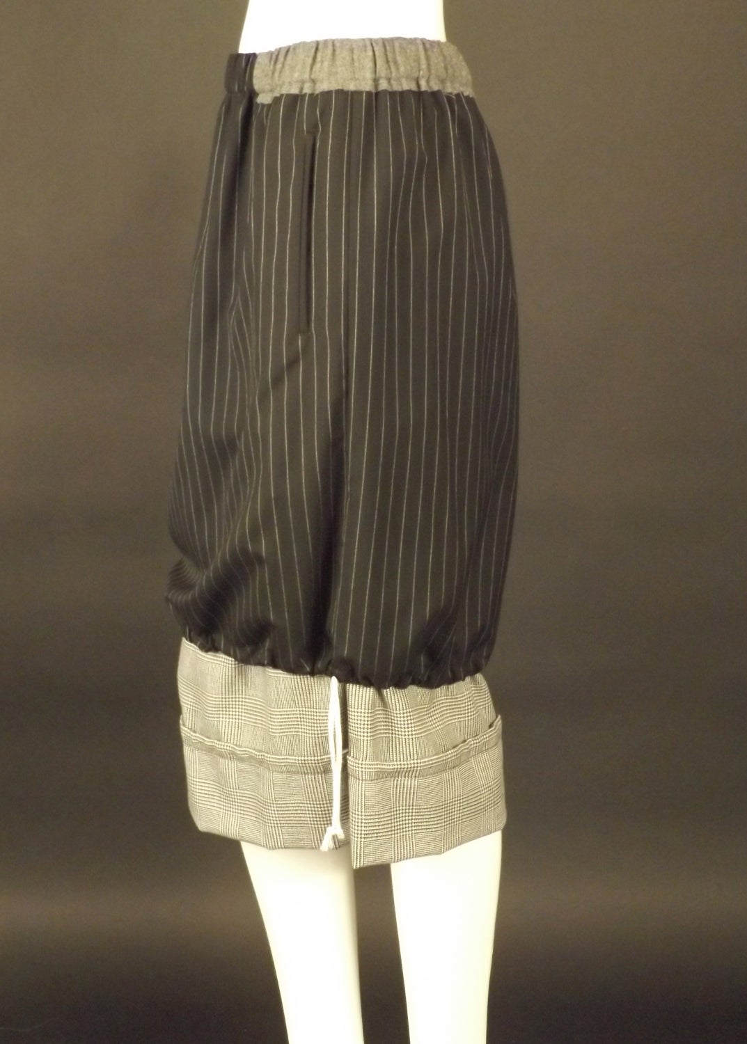 2008 Fall Collection. Fantastic skirt in contrasting wool suitings. There is a gray flannel waistband a pinstripe skirt and a black and white houndstooth plaid under skirt. The waistband is made of an elastic casing. Drawstring ties at the hems of