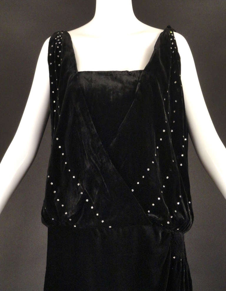 Gorgeous c.1920 evening gown in black silk velvet and dotted with sparkling rhinestones. The bodice crosses in front with a plunging neckline in front and back. The bodice is open down the sides to the dropped waistline. Underbodice or chemise is