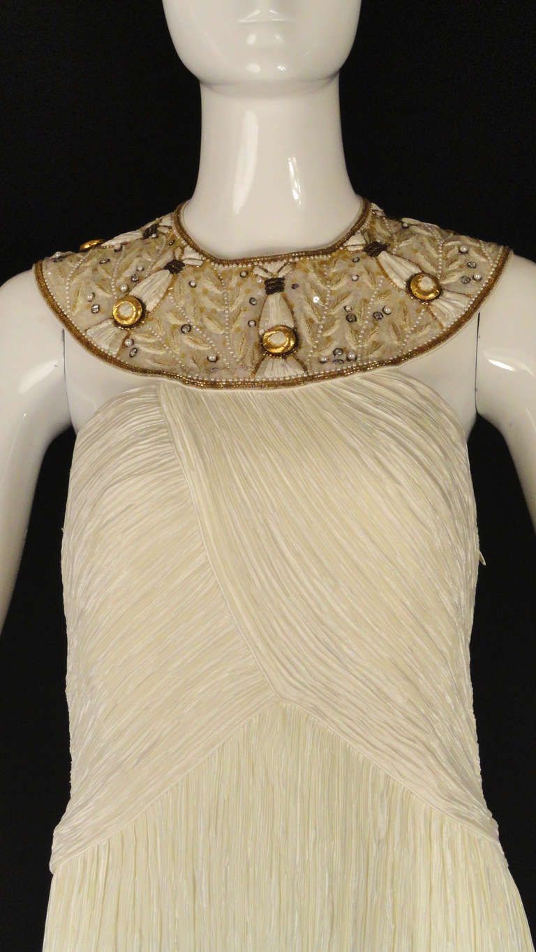 1990s evening gown in an off white, poly, crinkle pleat. Amazing Egyptian collar in organza that is heavily embroidered and adorned in pearls, gold beading, rhinestones and clear aurora borealis sequins.  Side zipper closure.