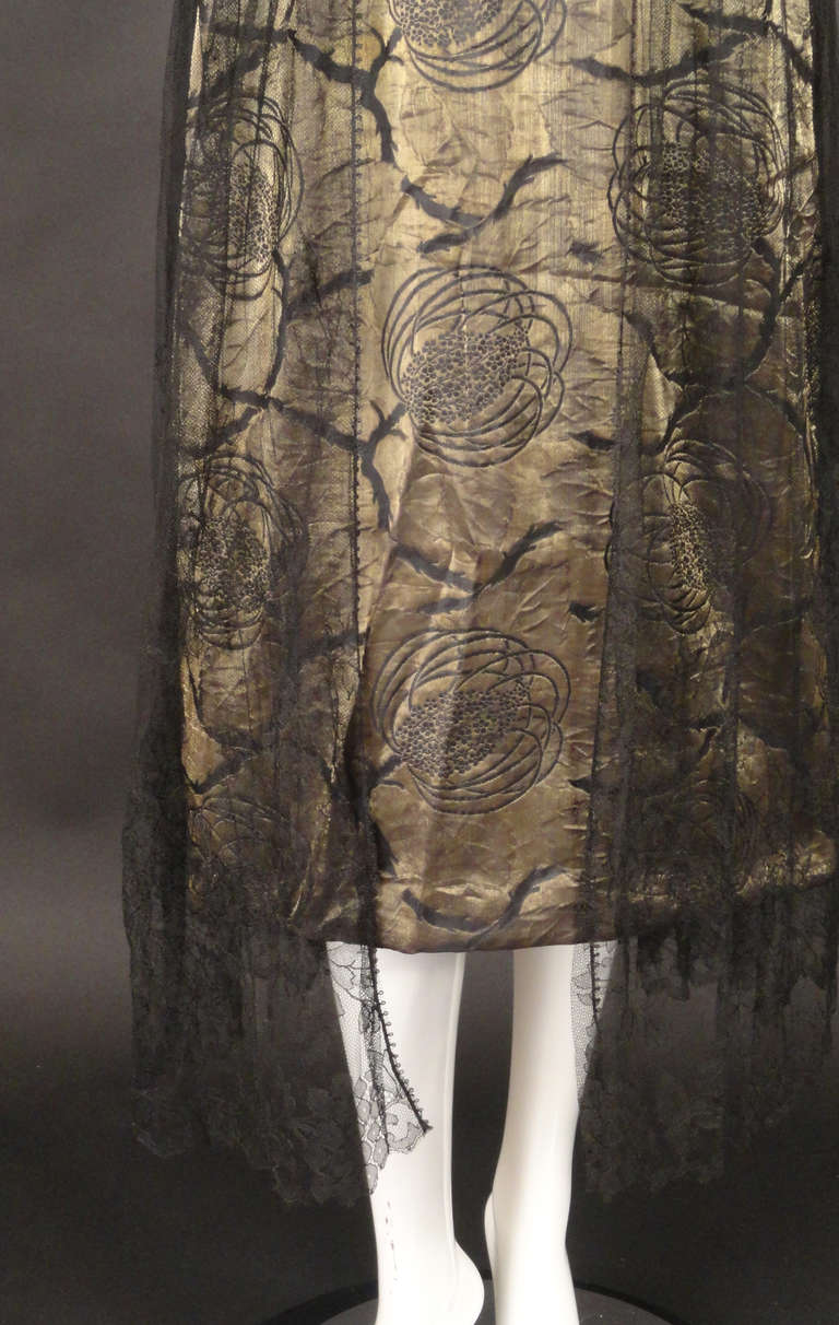 c.1920 Evening dress in gold bullion with a gorgeous nouveau floral design. The gown has a fly front bodice with double straps.  The bodice is pleated and wraps at the back. Gored skirt falls from beneath the bodice at the slightly dropped
