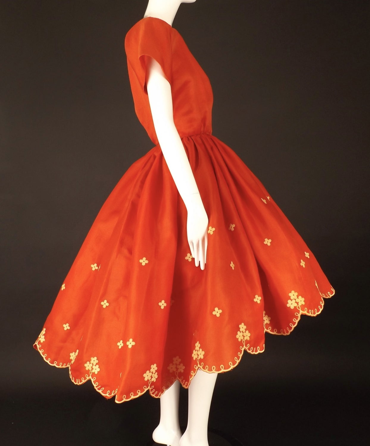 Gorgeous early 1960s party dress in a red silk gazar.  The bodice has a wide, scoop neckline with a blouson at the waist. No darting at the bust. Short sleeves are cut in one with the bodice. The back is slit down to the waist and has a single