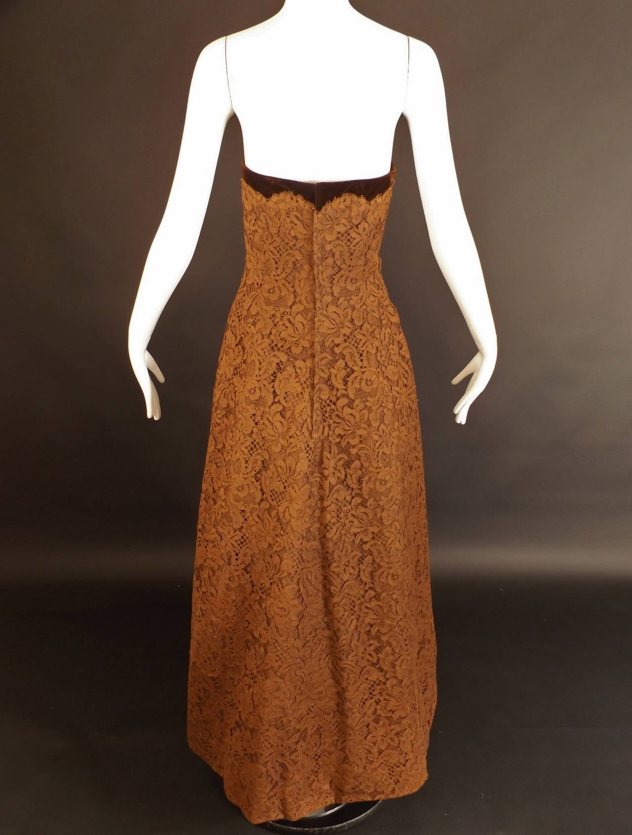 Gorgeous early 1960s evening gown in rows of brown floral lace appliquéd to itself and with a lining in a brown rayon faille.  Brown velveteen edges along the top of the boned bodice and runs down the center front. A large bow adorns the front