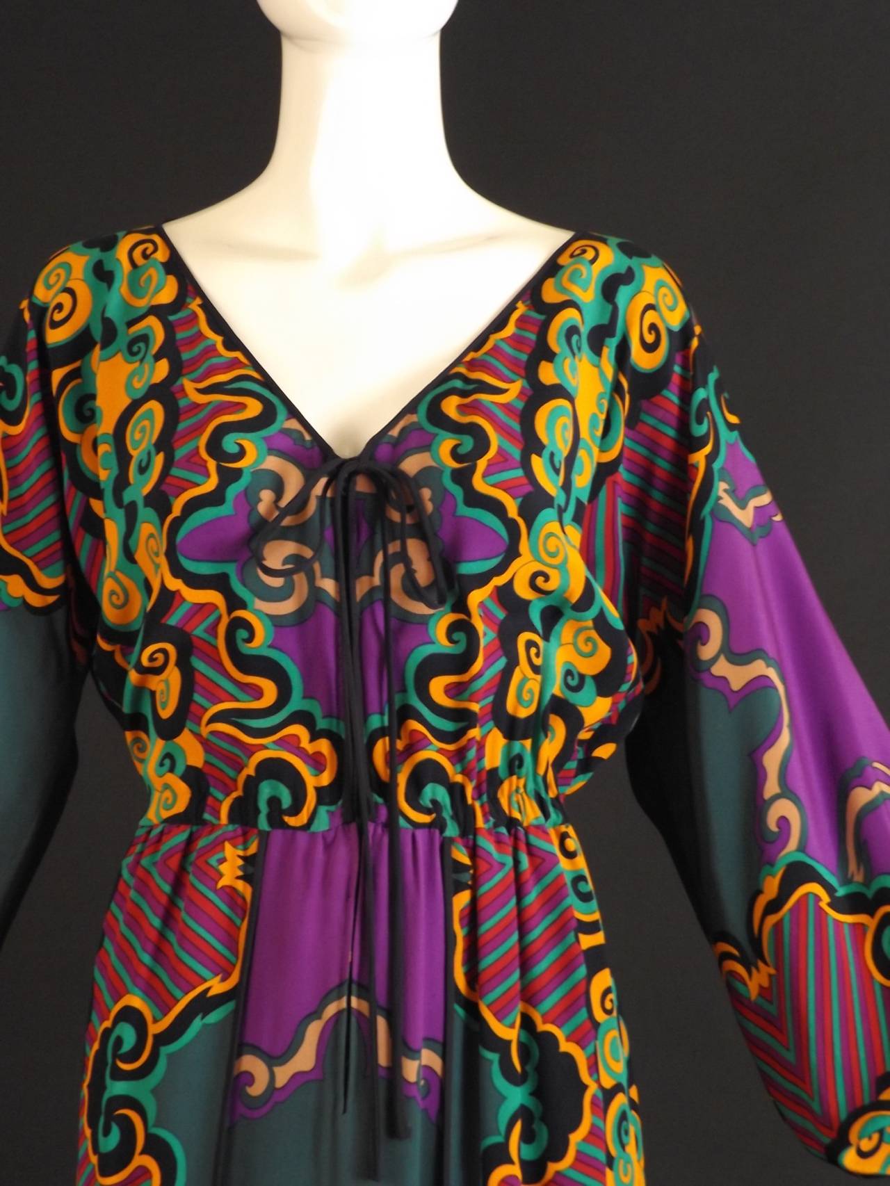 Gorgeous 1970s maxi dress in a fine printed silk in green, purple, yellow and black.   Zipper closure down the front with string ties at the base of the neckline. Elastic gathered at the waistline. Two panel skirt. The front wraps around to either