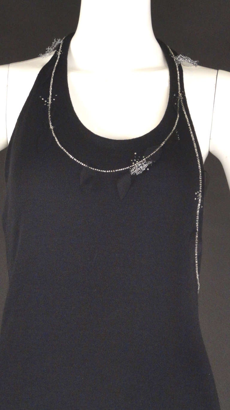 1990s Dress in a black wool sweater knit.  Scoop neckline with an asymmetrical design down the back.  Silver seed beads and tiny sequins edge the neckline and around the left side of the dress.  Petals in black and silver mesh are dotted along the