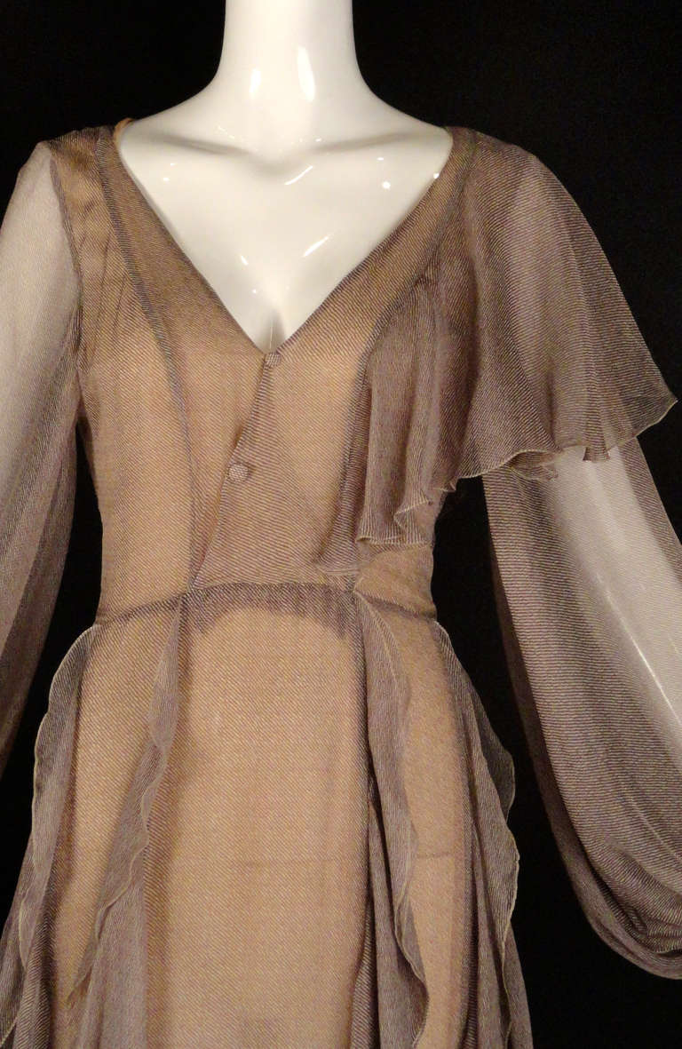 Early 1990s evening dress in a brown and cream silk chiffon pin stripe.  Wrap front bodice with decorative buttons. Single bias ruffle crosses over the left shoulder. Long, unlined poet sleeves end with bias ruffles at the wristbands.  Natural