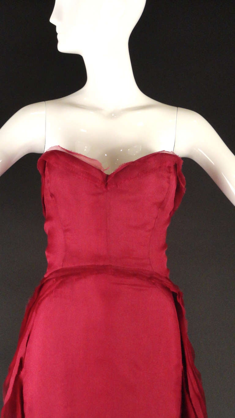 Stunning ball gown in a burgundy silk chiffon. The gown has a bustier bodice with an attached bustier girdle.  The gown is from beneath the waistline seam. Rows of chiffon ruffles begin at the front waist and then trail down the sides and flow in to