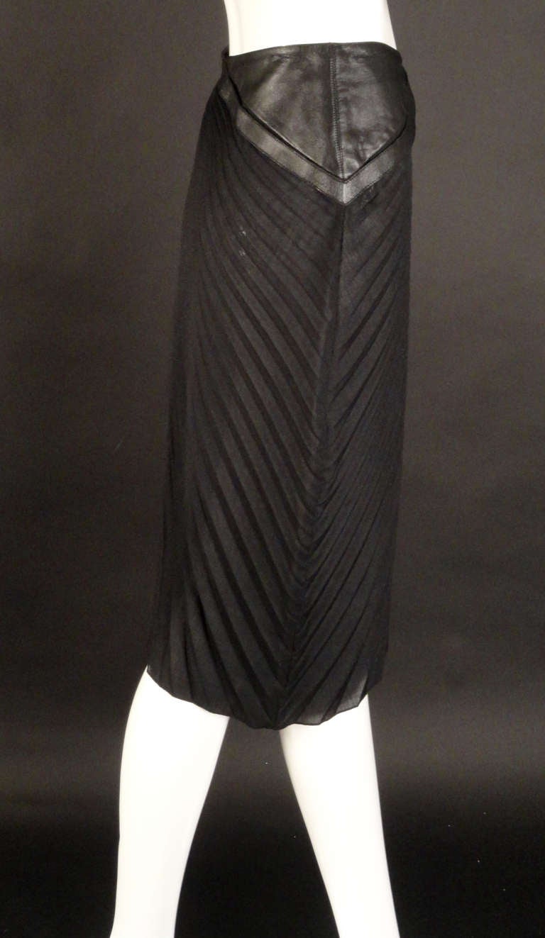 Early 1990 wool blend, accordion pleated skirt with a leather yoke and waistband. Working buckle on the left side waist with a cutout of the skirt beneath. The skirt is curved around the hip down the right side and cut straight on the left side. 