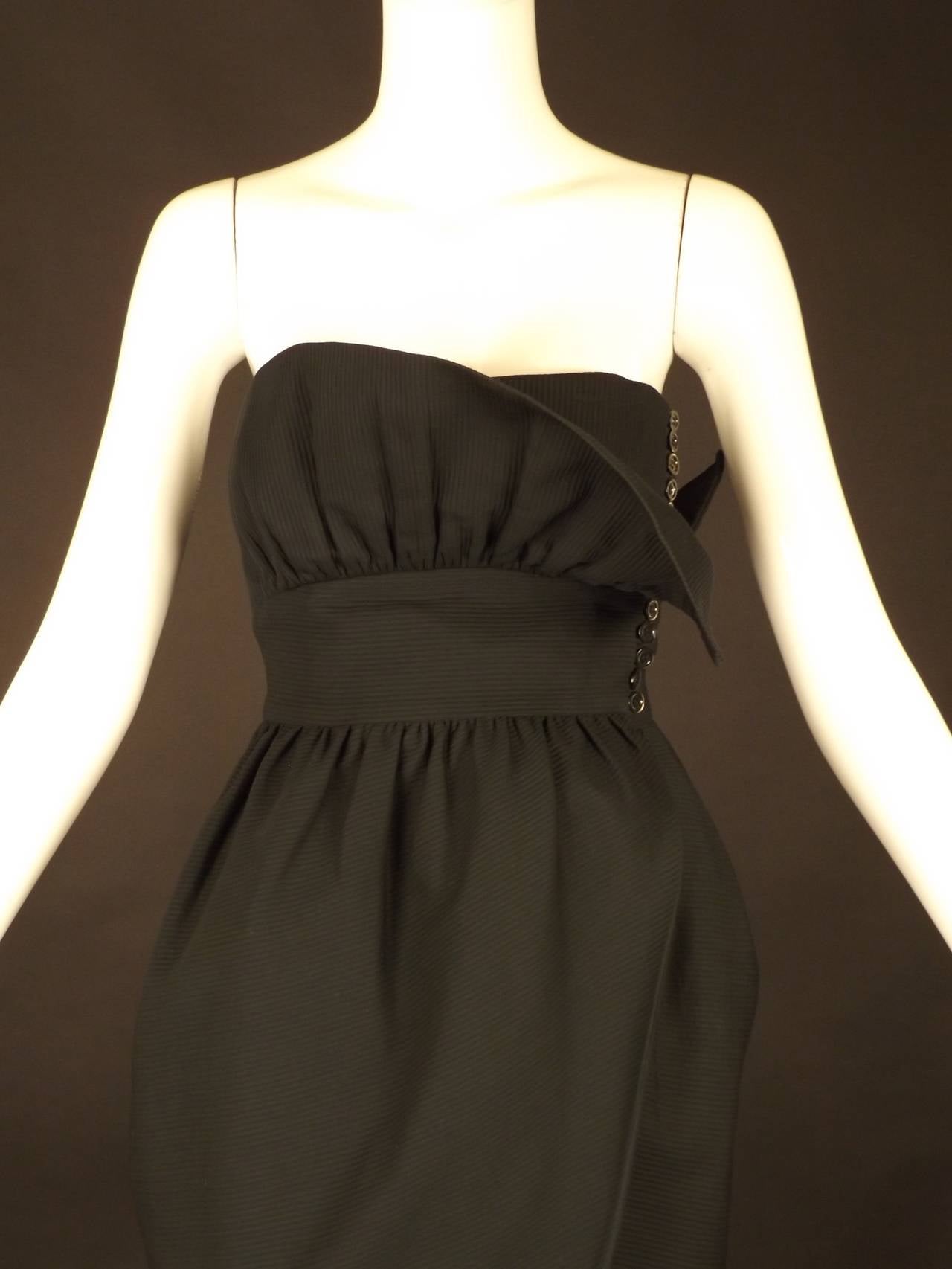 Adorable 1990s cocktail dress in a black ribbed cotton. The dress wraps across the front with button closures down the left side. Strapless with a midriff yoke and a dart fitted bodice. The front overlap is gathered creating a standing ruffle across
