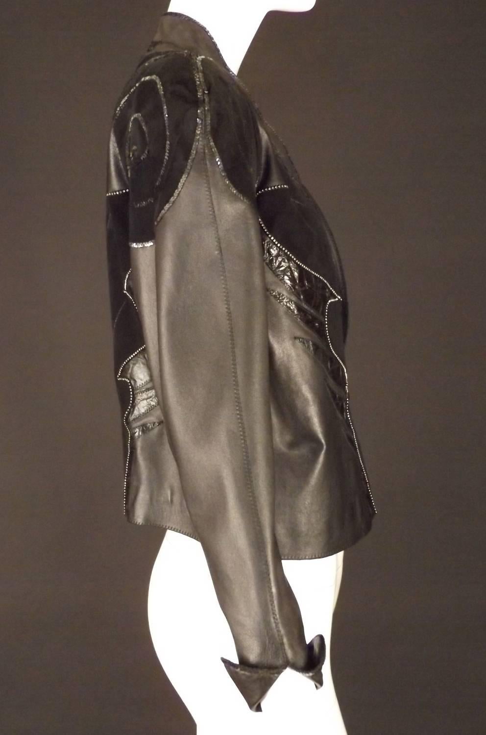 Awesome 1980s oversized jacket in black leather. Fluted shawl collar with a single button and loop closure at the front waist. Large shoulders and upper sleeves taper to the wrists with turned back cuffs. The jacket is adorned in appliqués of black