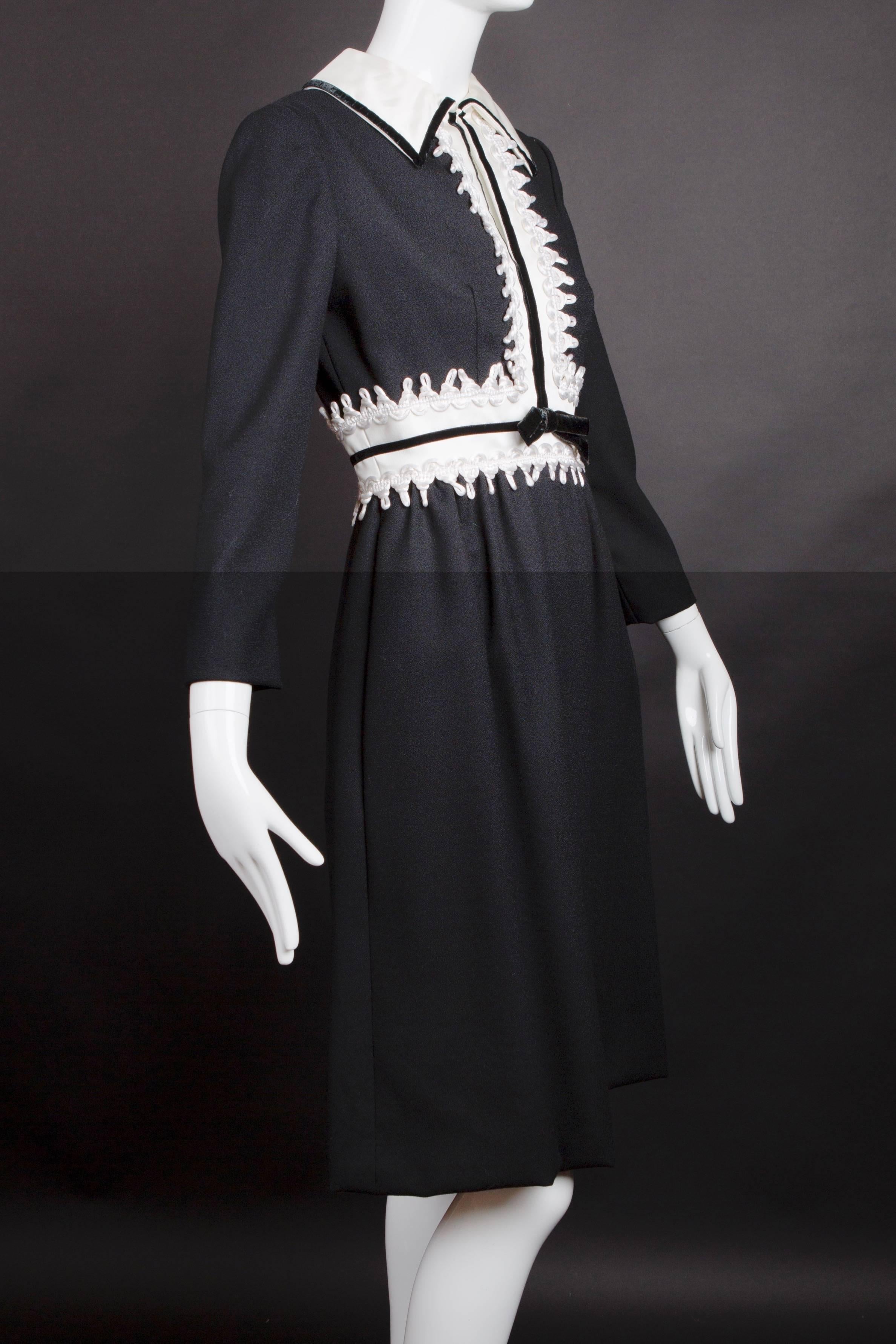 Adorable late 1960s dress in a black wool crepe with an appliqué waist and center front panels in white satin trimmed in white loop cord. Black velvet ribbon edges the collar, center front and waistline seam. The dress is dart fitted from the bust