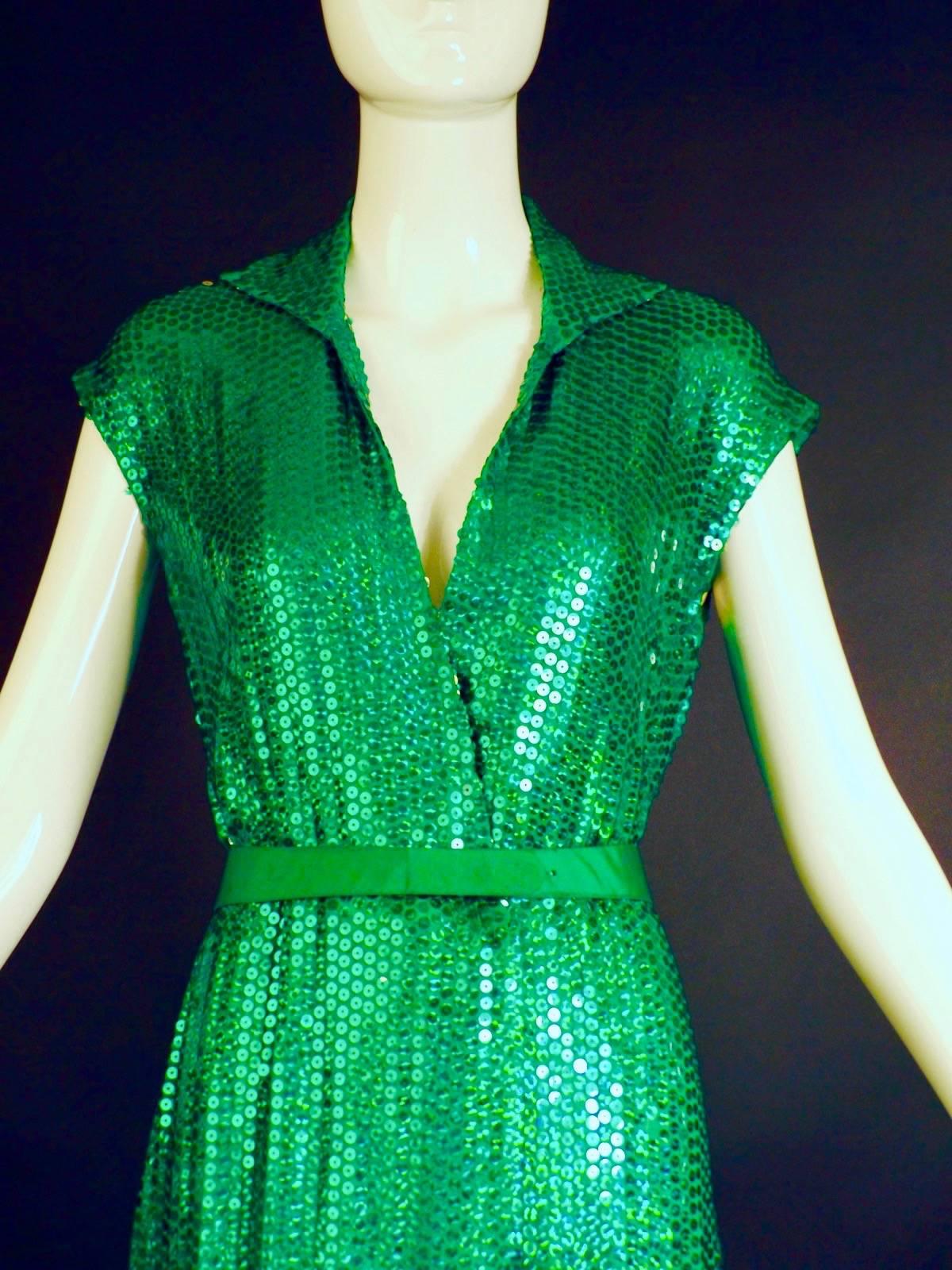 Stunning late 1970s evening gown in green hologram sequins on silk chiffon. The gown has a wrap front with hook and snap closures. Spread collar that also stands around the neck.  Wide, green satin belt has snap closures.  The gown is lined in silk