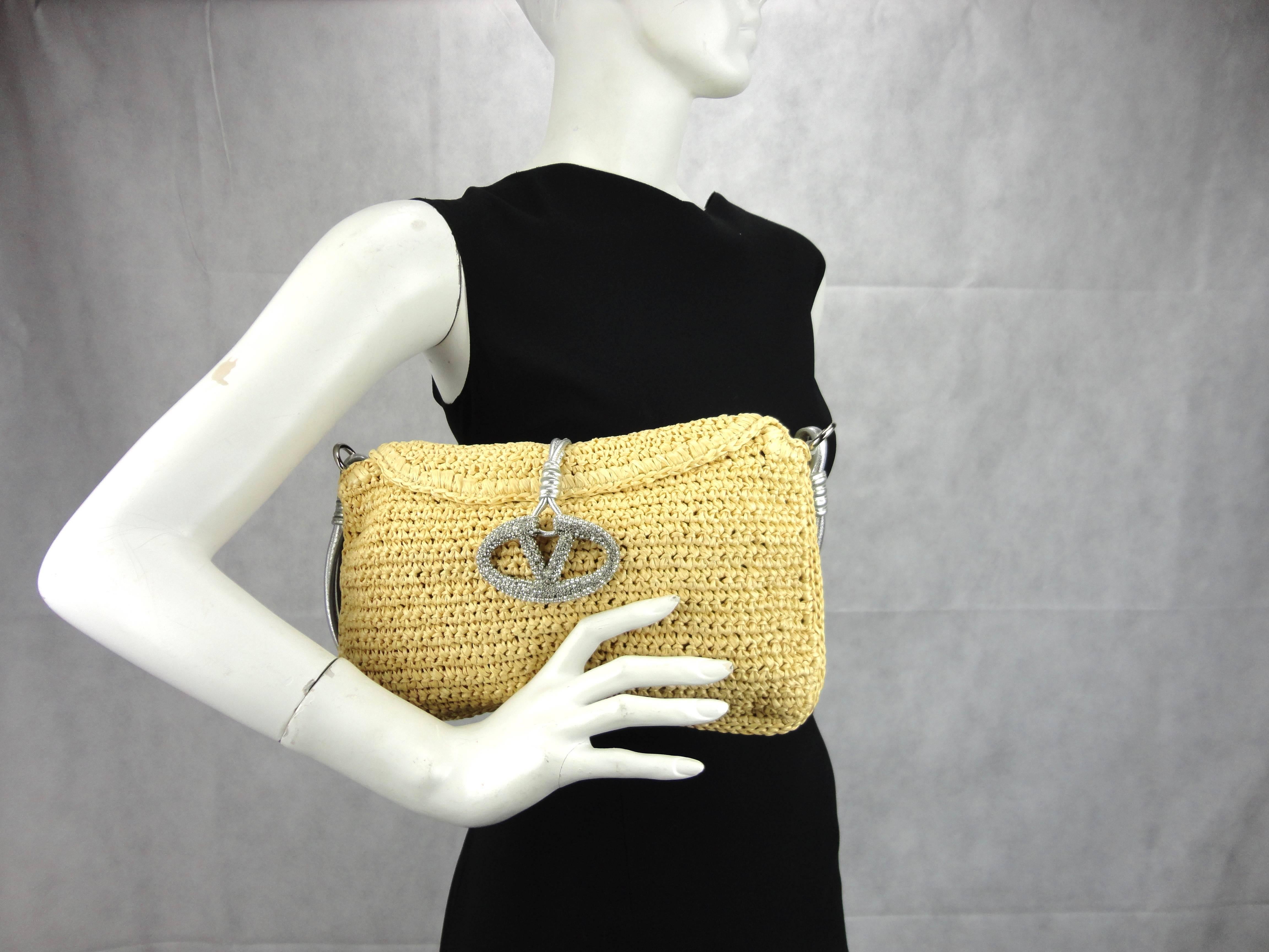 Valentino Tan straw (raffia) bag with silver leather strap and front flap closure with Valentino logo in Strass. Interior zip pocket. Mint condition.

Measures: H 21 cm x W 30 cm 