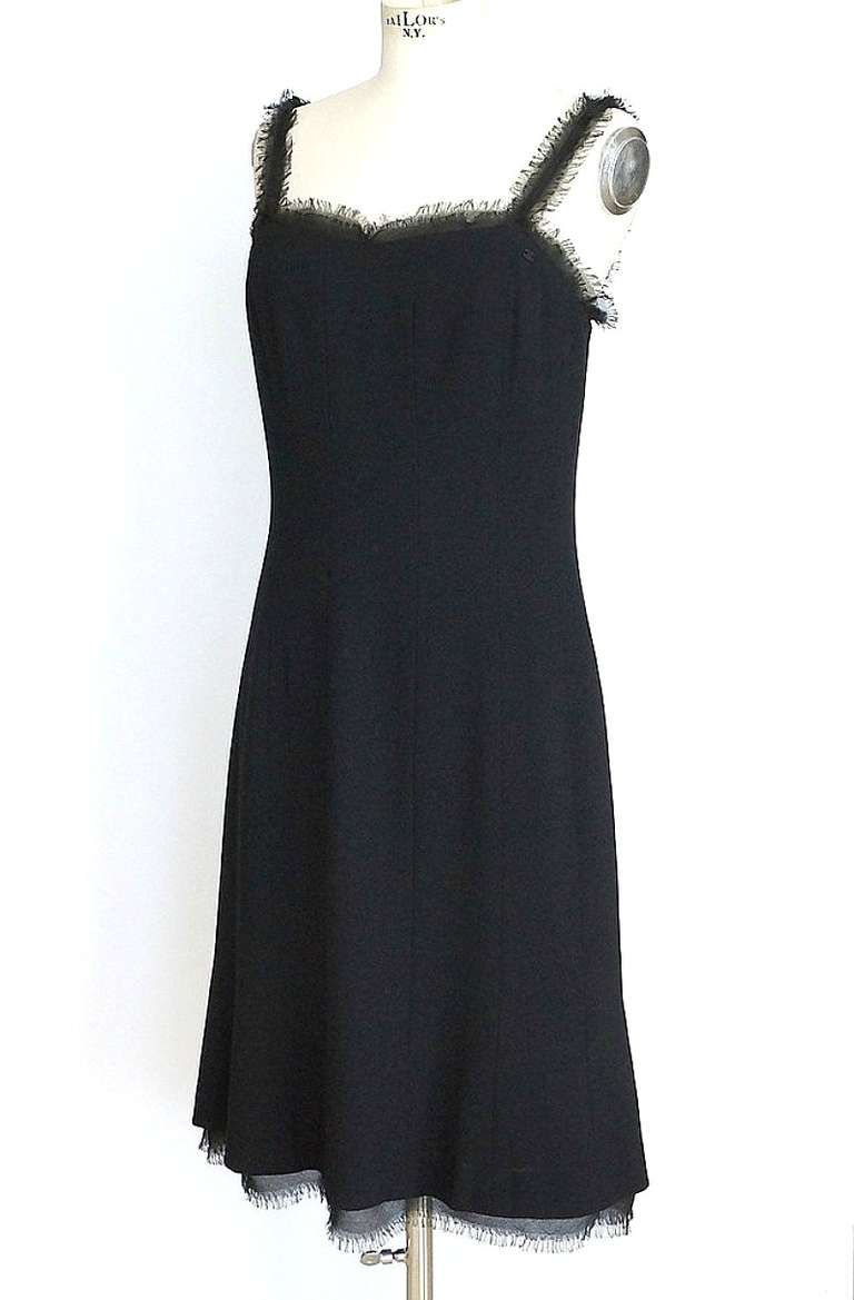 Guaranteed authentic CHANEL 04P exquisite black dress with subtle chiffon detailing.
Dress is edged in signature CHANEL silk chiffon fringe.
Hidden zipper in back. 
Dress is subtle A line.
CHANEL diamante logo on bodice.
Fully lined in