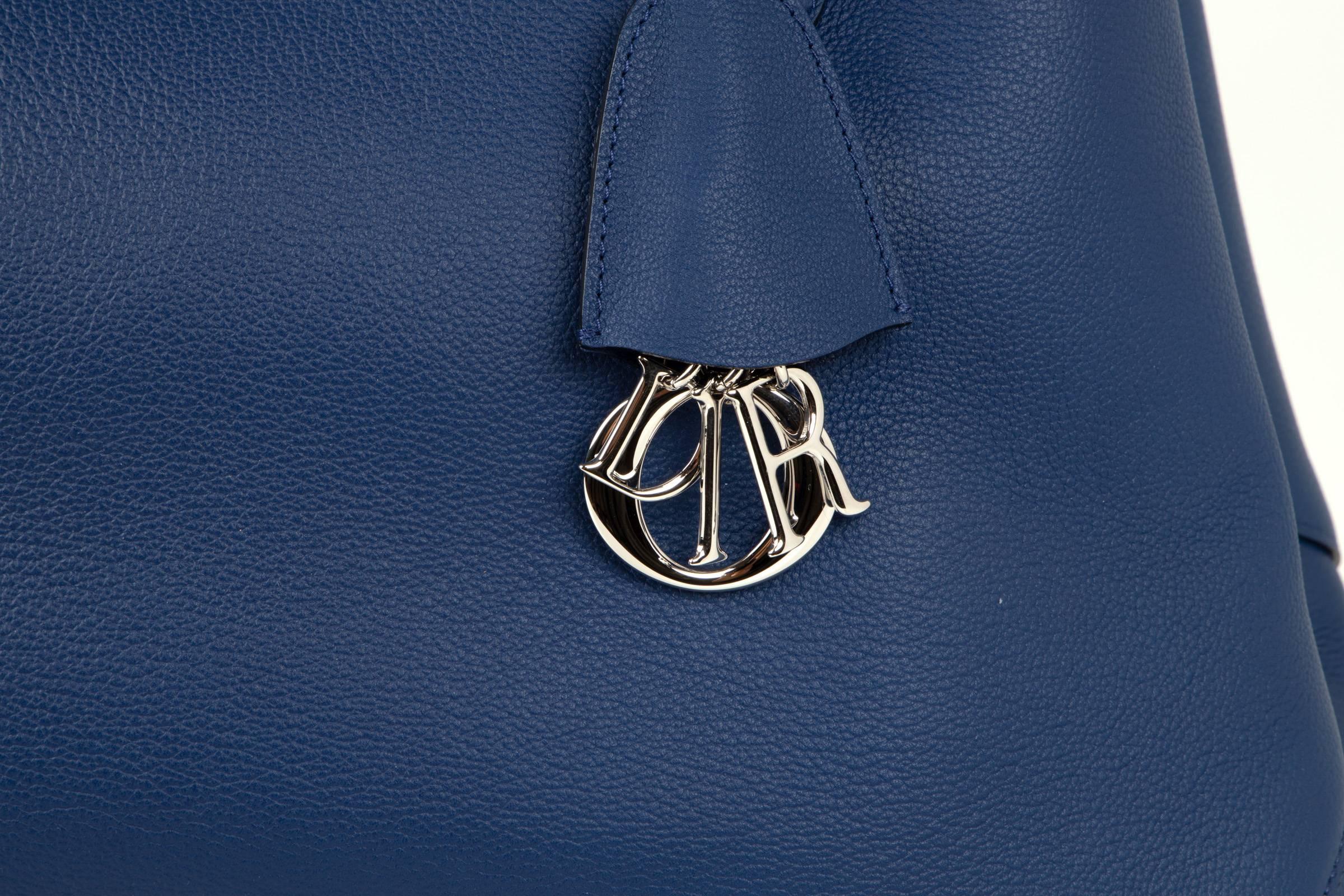 Guaranteed authentic Christian Dior Blue Open Bar tote bag.
Rich vivid blue with contrasting light blue interior. 
Clochette reveals the iconic Dior charms.
Tote has straps inside with silver turn key. 
2 interior slot pockets and 1 snap pocket for