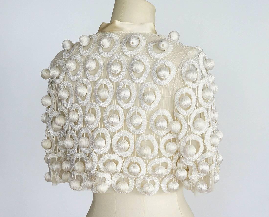 Guaranteed authentic OSCAR de la RENTA  smashing one of a kind evening jacket.  
Cream tule 3/4 sleeve short jacket.
Embroidered circles with hanging 'balls' throughout - the effect is striking.
Neck is trimmed in silk taffeta with a long