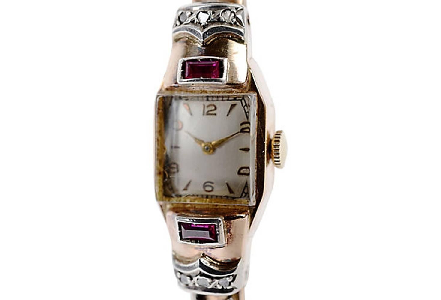 18K yellow gold ladies' watch featuring 14 single-cut diamonds and two rectangular rubies set in white gold. Marked: 18K. The bracelet is a spring-loaded cuff with a safety chain. The Swiss works are manual wind and marked 21 jewels. In running