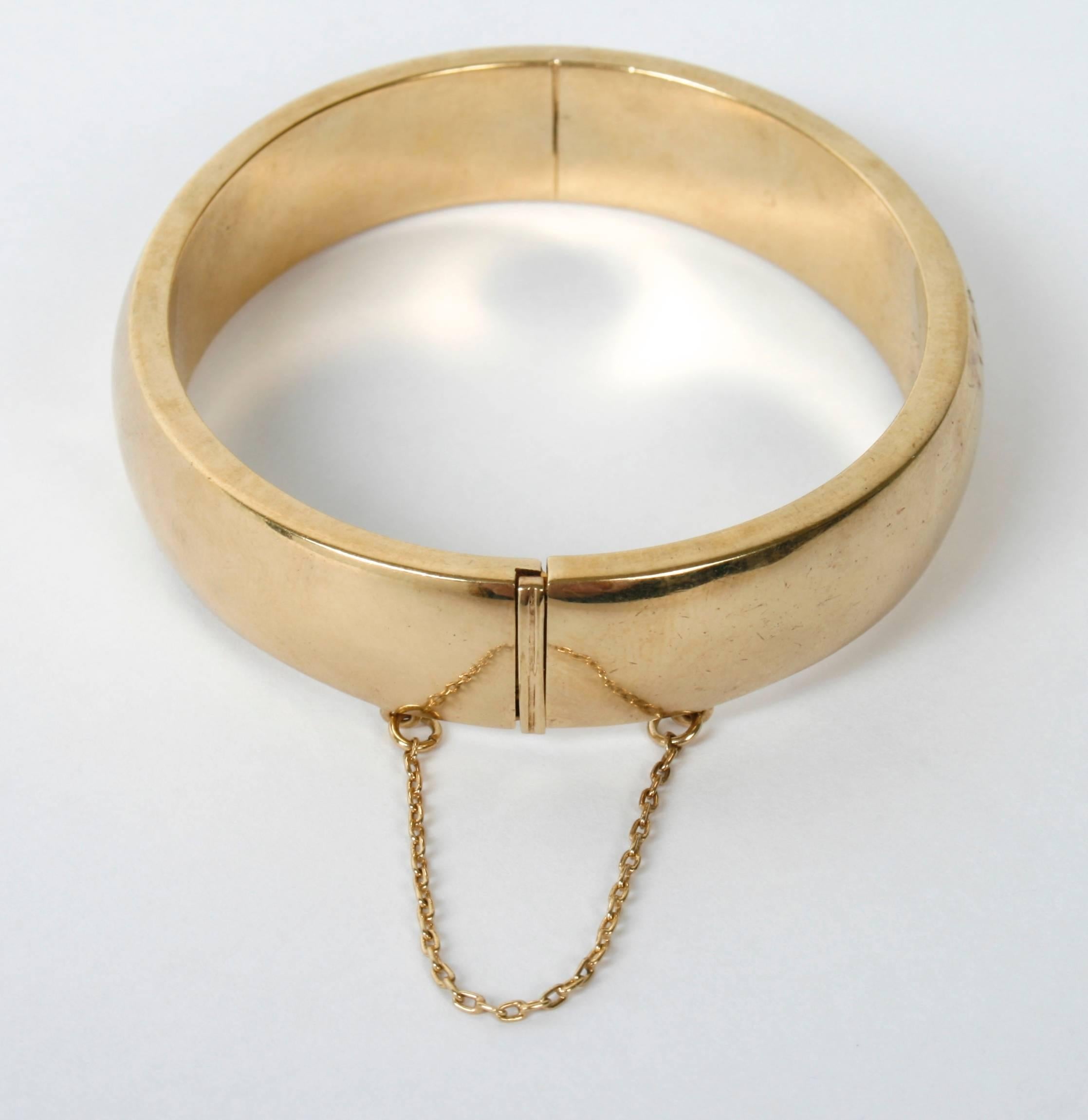 This gold plated sterling Silver bangle bracelet has an oval shape with squared off sides. It opens with an invisible hinge and a secure clasp that releases with a narrow push-bar. It also has a safety chain. The bracelet is marked ''925.'' It has a