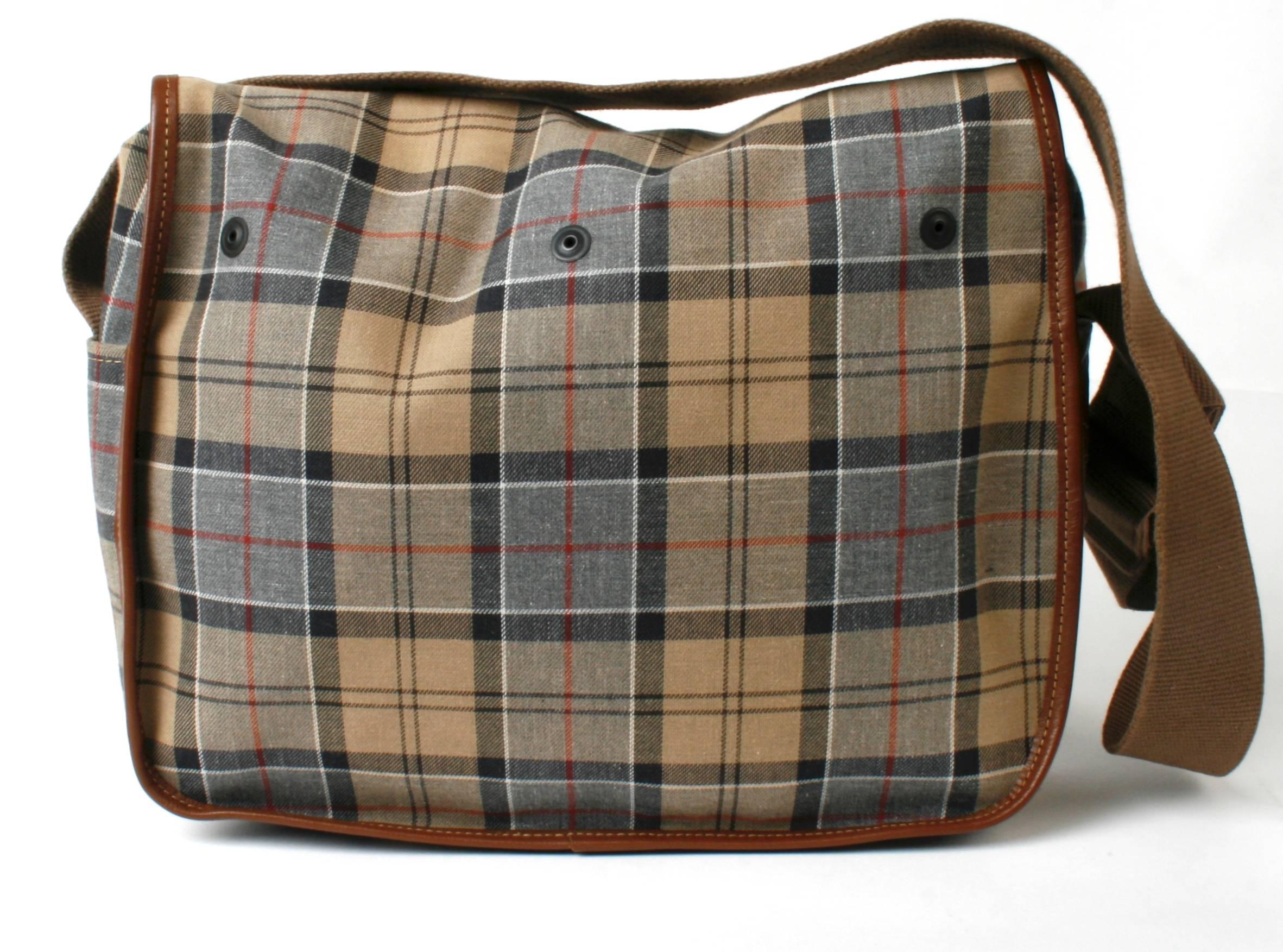 Barbour Medium Tarras bag in Dress Tartan waxed canvas. It is trimmed in brown leather with antique brass buckles and hardware.  Adjustable cotton webbing shoulder strap and two large bellows pockets with signature snaps and grommet holes. The side