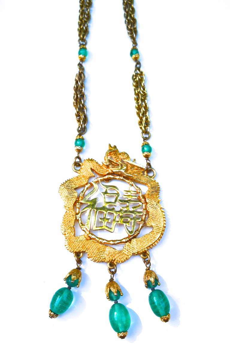 1970s Kenneth Jay Lane Asian influenced necklace featuring a pendant with a large dragon, script, and glass bead fringe, signed. Layered chunky style chain. Great scale and vibrant green accents.