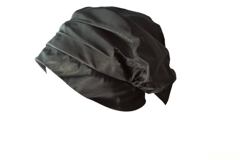 This Amy New York hat has a sort of turban or wrap style, that is unique and sits to the side per design. It can be adjusted a bit. The back has a some stretch and a fun tie applied. It has no faded spots on the black. Feels like a rayon organza.
