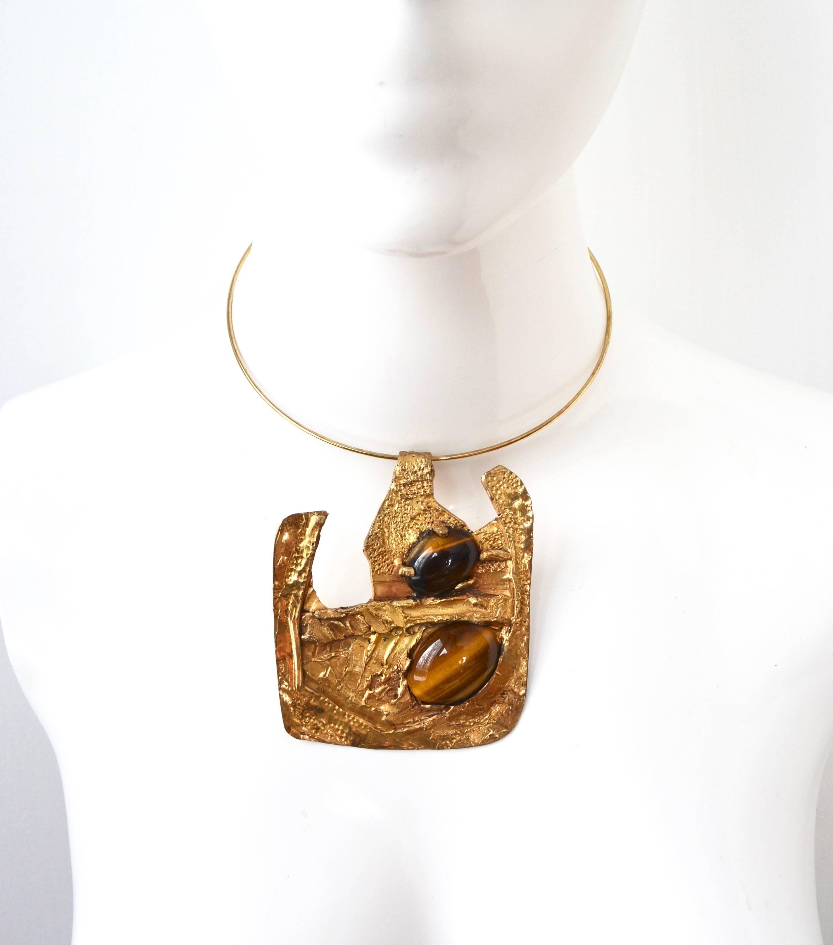 Oversized brutalist style gilt metal and true tigers eye stone pendant on a collar style choker. Good condition, mild finish wear on the back mostly. 3.5″ long x 3″ wide. About 16″ around. unsigned.