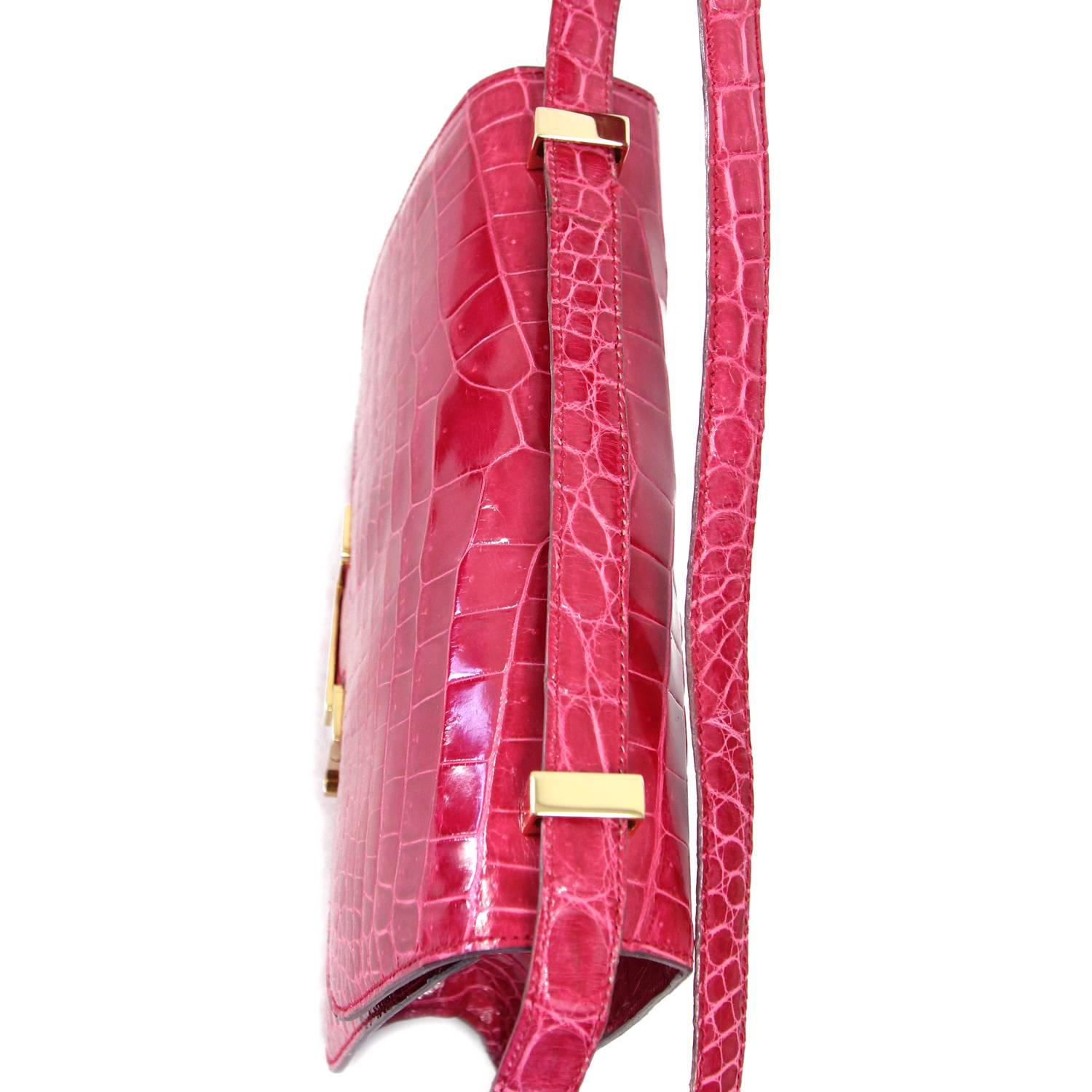 Vivid fuchsia crocodile leather crossbody bag made by Corradi Parma with golden hardware. The bag is inspired by the iconic Hermès Constance bag and shows a metal "H" snap lock closure. The item comes with a small purple leather wallet. It