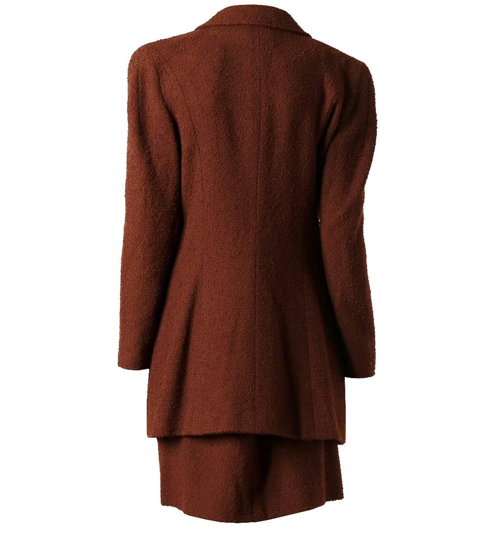 Characteristic Chanel wool blend suit in a brick red color. The jacket shows a classic collar, hidden frontal closure, four buttoned pockets and long sleeves. The knee length skirt has two small pockets and a hidden zip closure on the back. The item
