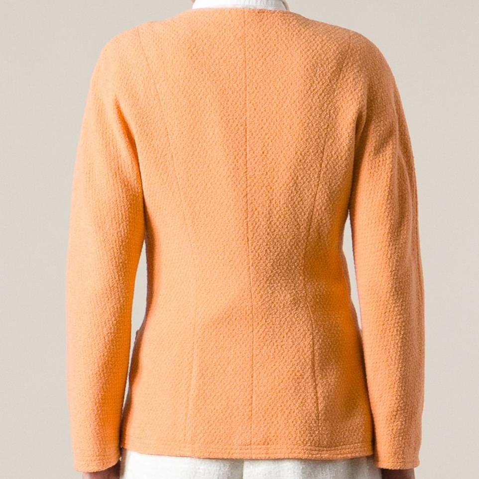 Chanel round-necked jacket in a pretty orange melon color with a row of eight logoed golden metal buttons on the front. It features four symmetrical frontal pockets, two smaller and two bigger. The item is vintage, it was produced in the 80s and is