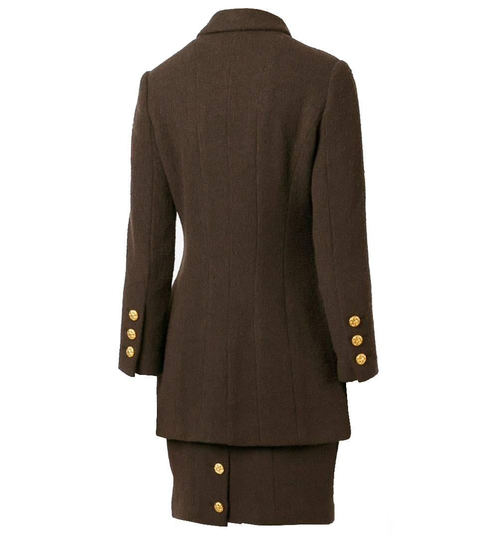 Classic two-piece skirt and blazer suit by Chanel, in brown wool. It features long sleeves, a front button fastening, front flap pockets, a full lining and button cuffs. The skirt features a knee length and a scarf collar detail, zip closure on the