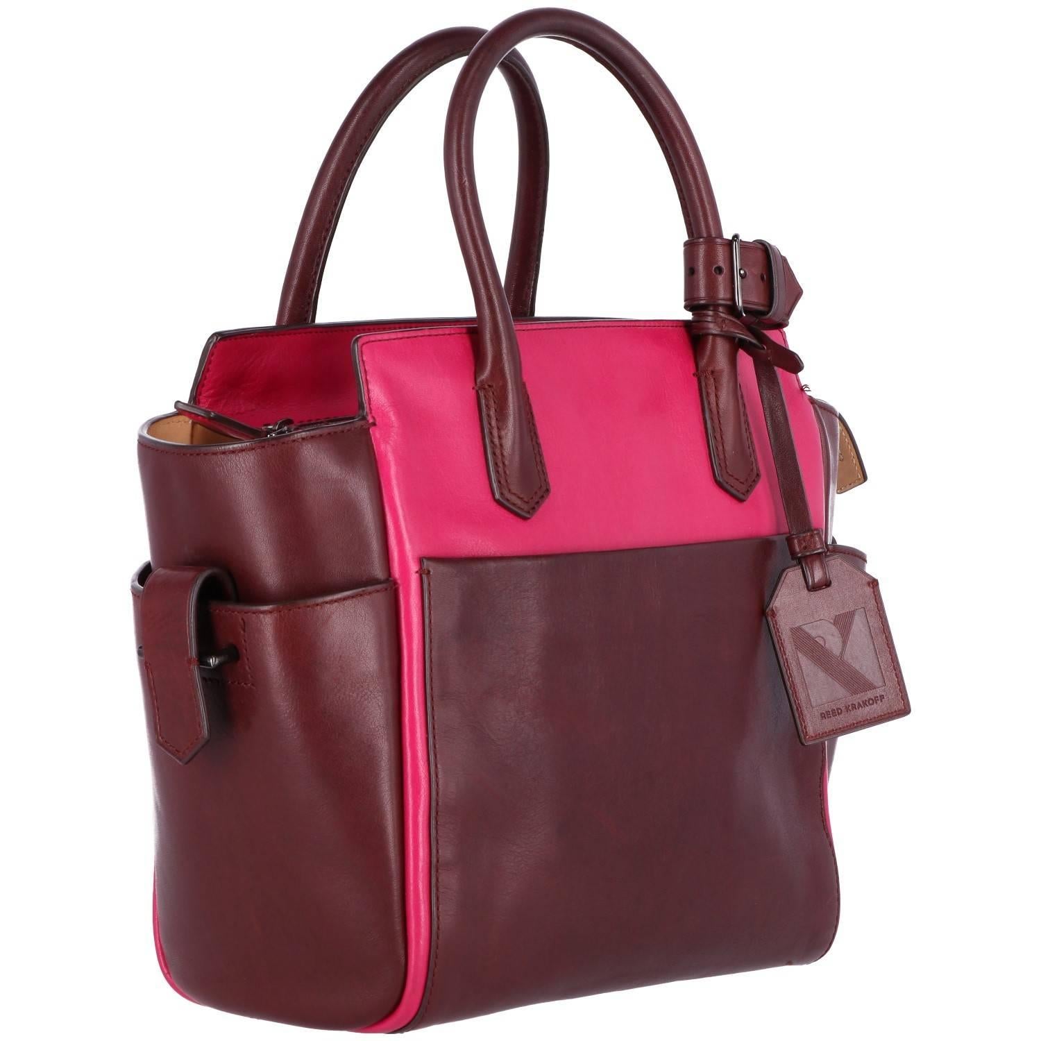 Reed Krakoff bag in a brilliant magenta leather. The inside lining features a zipped pocket and two open pockets. Also features three pockets on the outside and zip fastener. The bag comes with its address tag and belt for keeping the handles