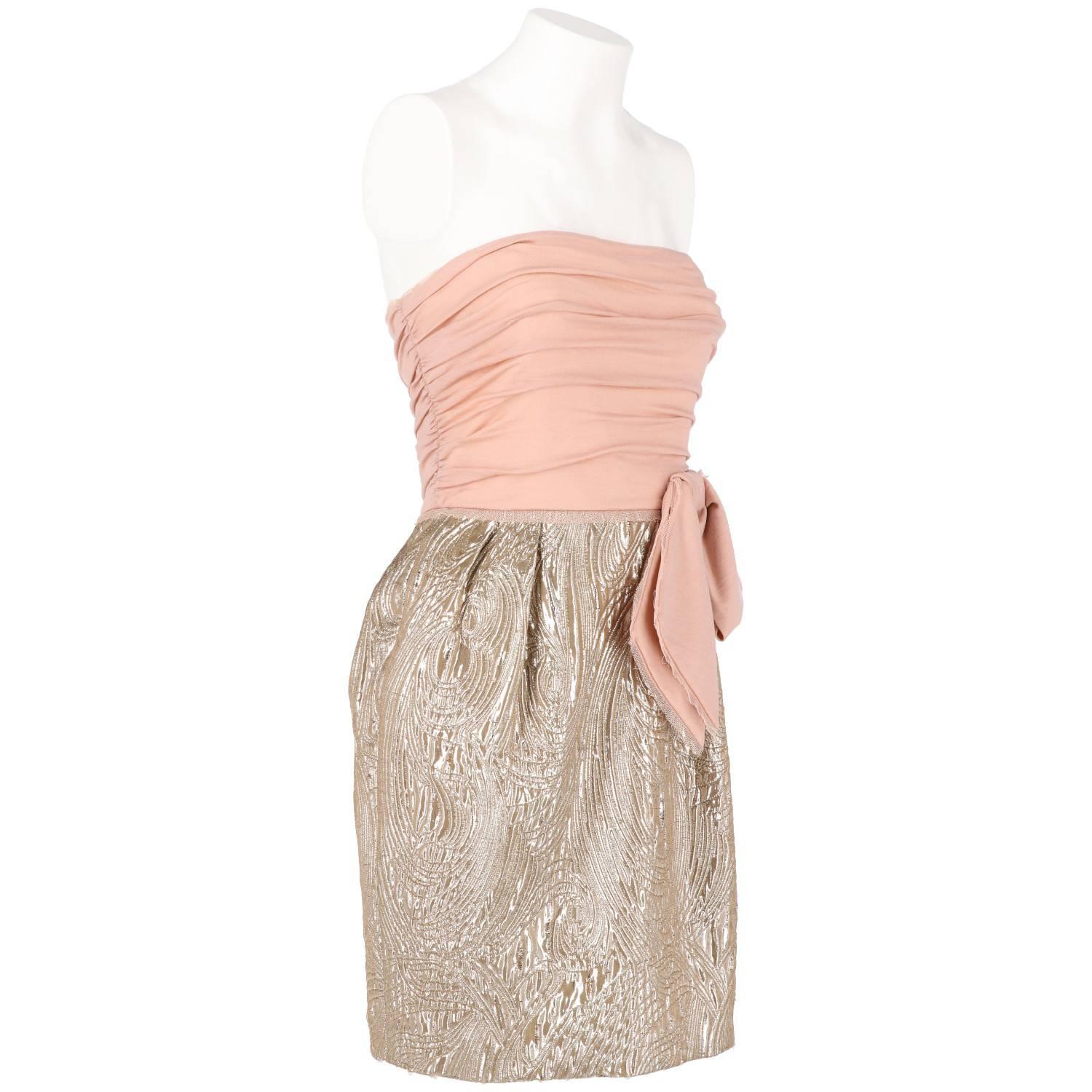 Elegant short vintage dress by Emilio Pucci. It features a pink sleeveless draped top with a large asymmetrical bow on the waist, and a ballon skirt in silver brocade lamé fabric. Lateral zip closure. The item is vintage, it was produced in the