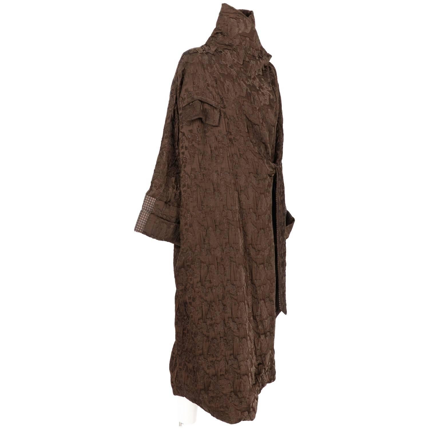 Antonio Marras majestic long baggy overcoat in brown jacquard fabric with inserts of a floral patterned fabric. It features a destructured asymmetrical shape, waistband closure and a button on the left shoulder. Lined in brown. The item is vintage